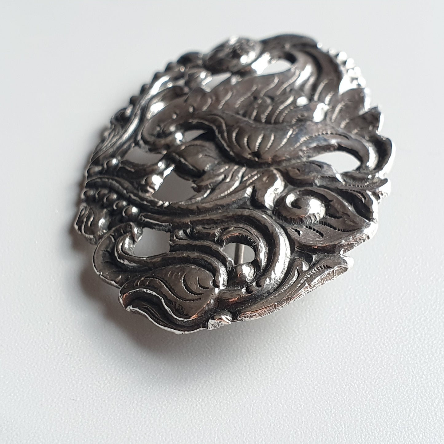 Ornate silver brooch with intricate floral and scrollwork design.