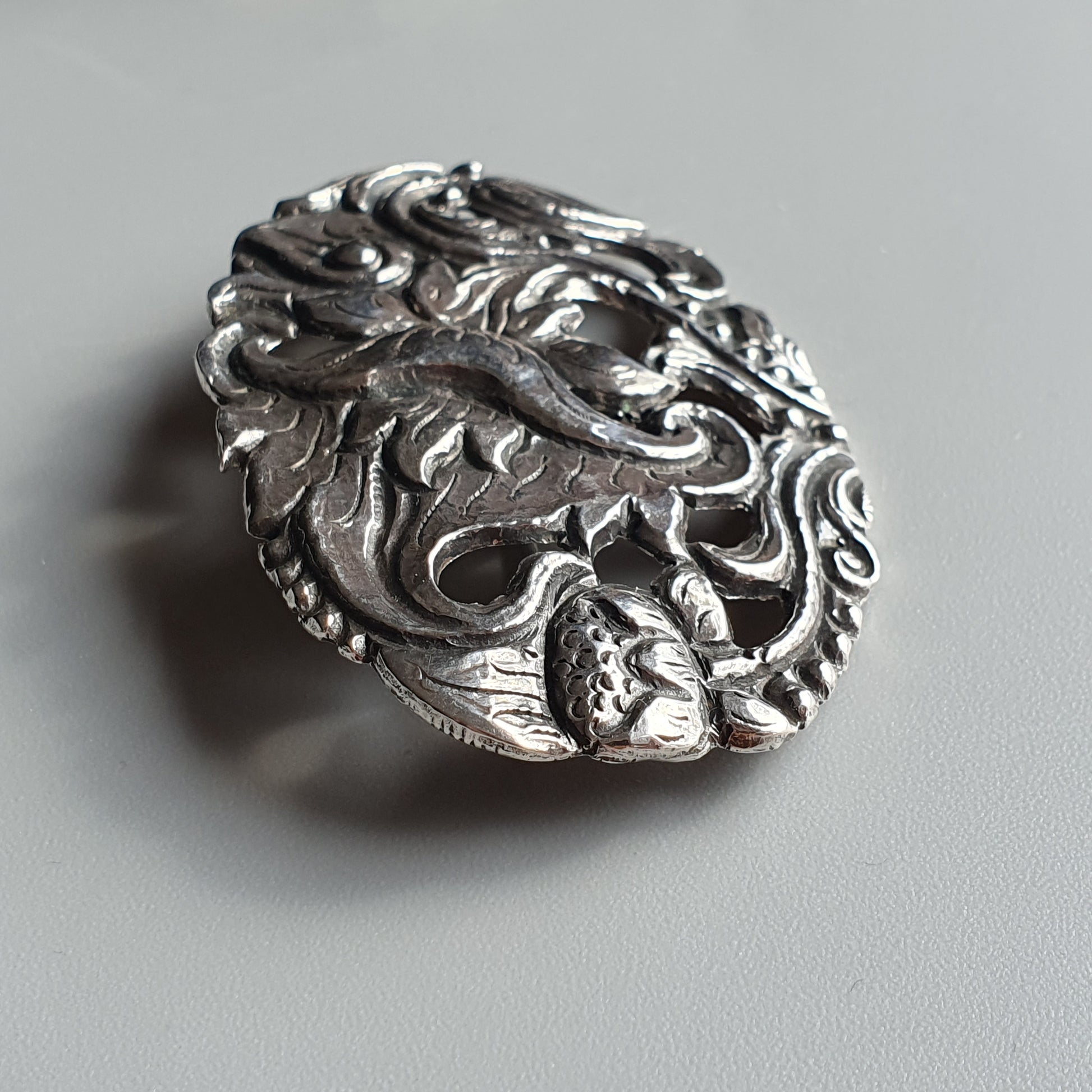 Ornate silver pendant or brooch featuring an intricate dragon design.