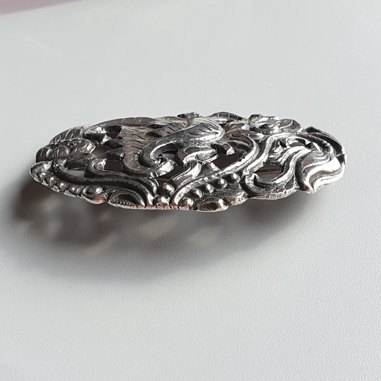 Ornate silver brooch with intricate swirling floral design.