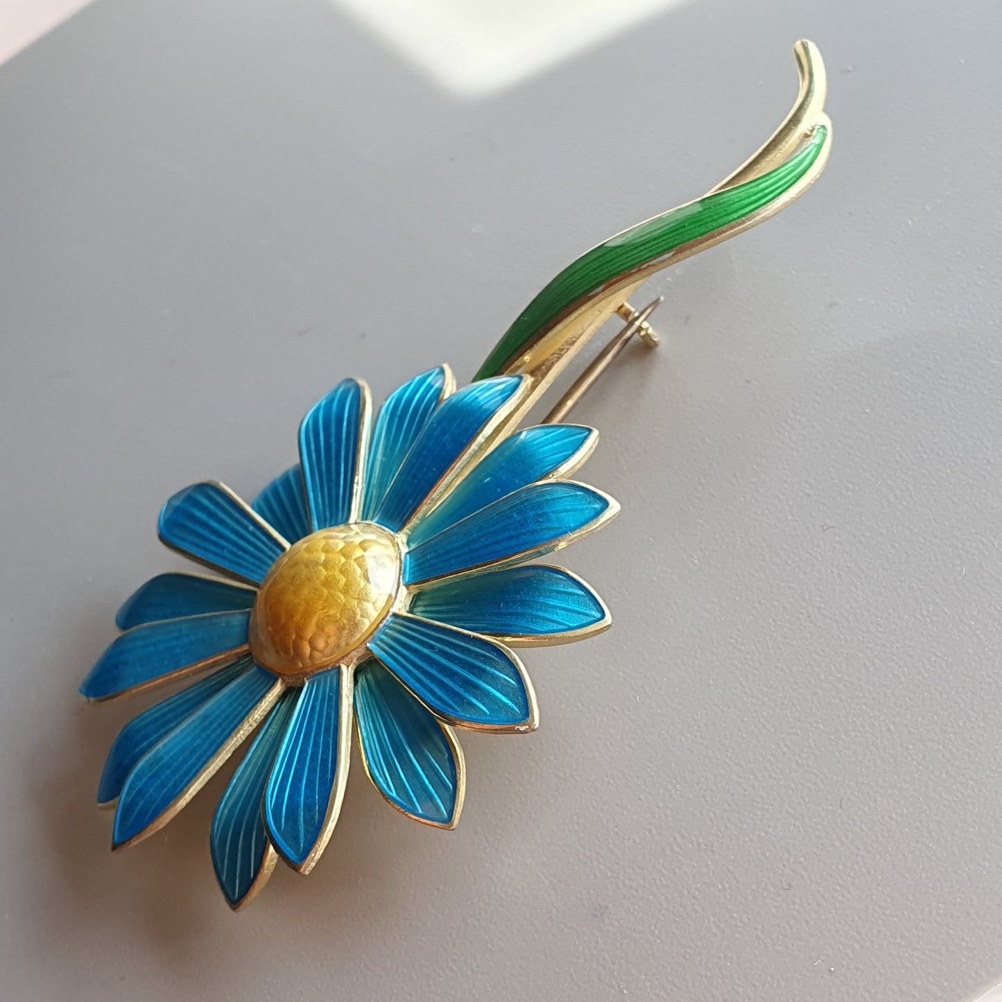 Vibrant blue and gold enamel flower brooch with a green stem.