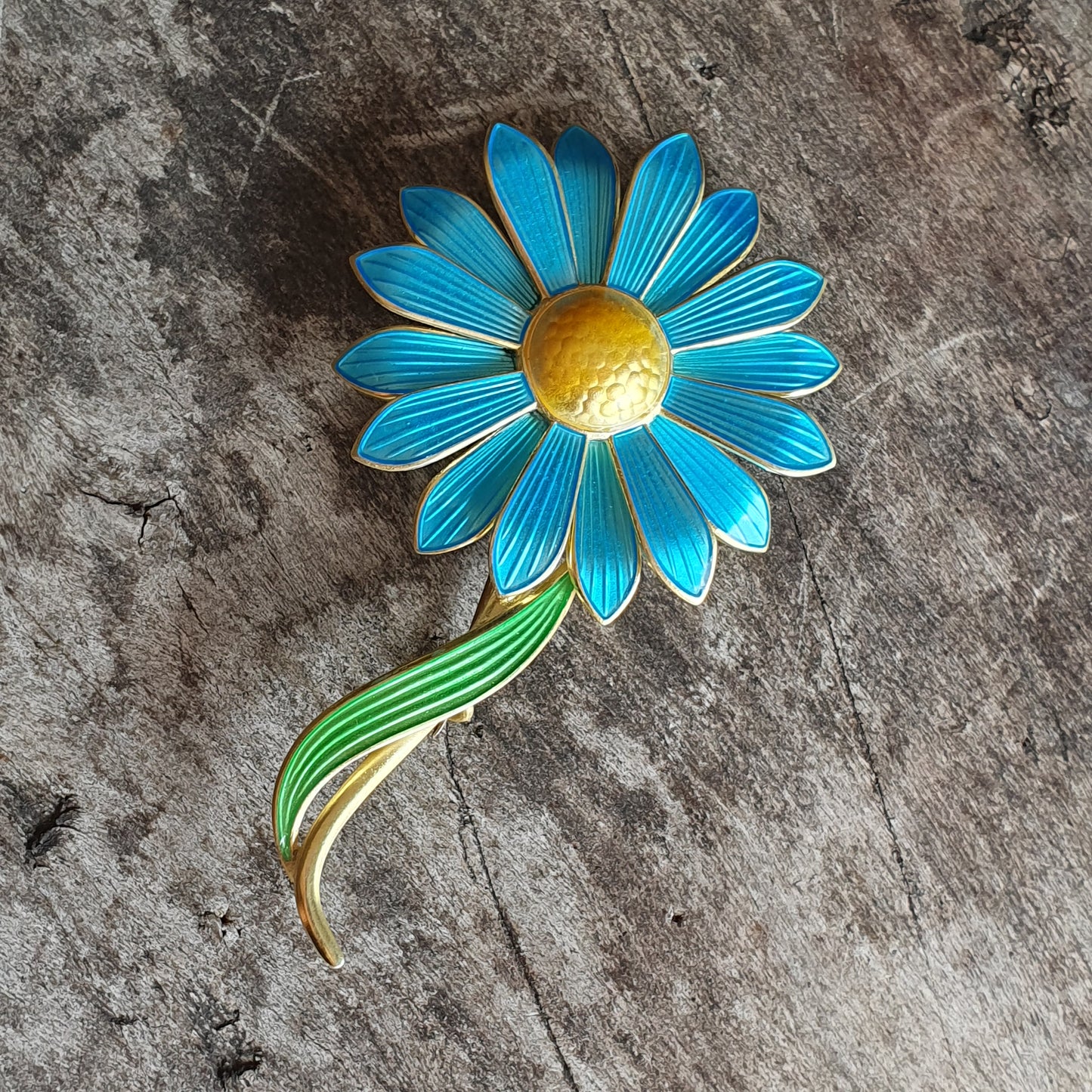 Vibrant blue daisy-shaped brooch with a yellow center and green stem.