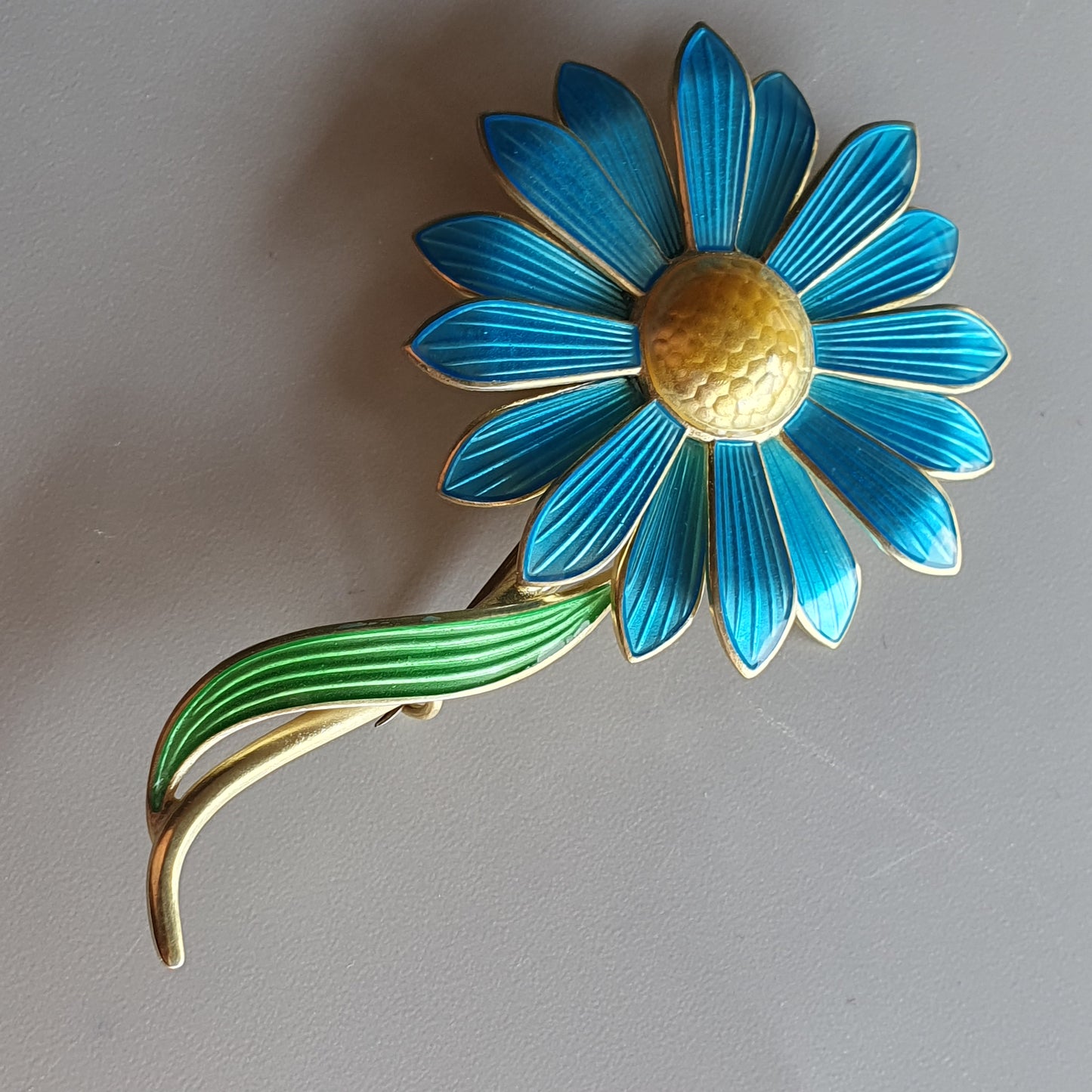 Vibrant blue daisy-like flower brooch with a green stem.