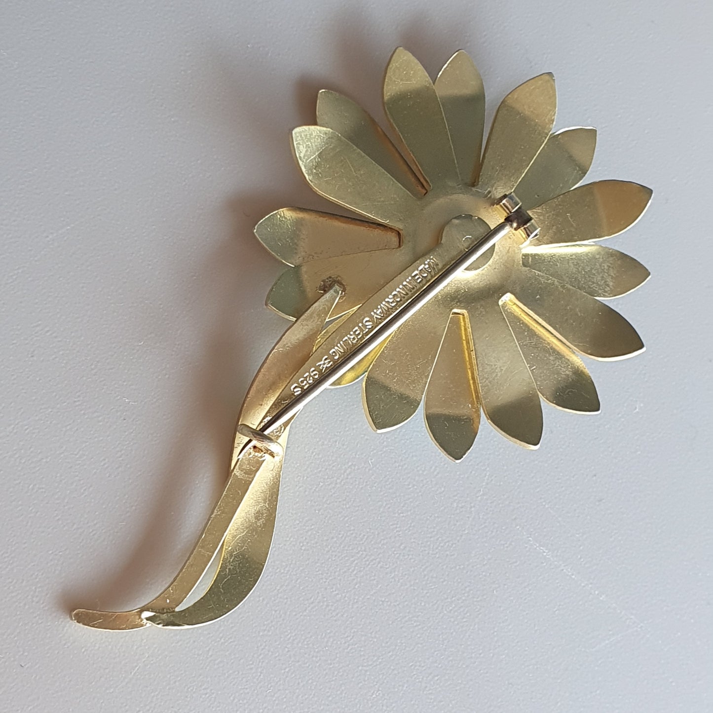 Gold-toned flower-shaped brooch with petals and a stem.