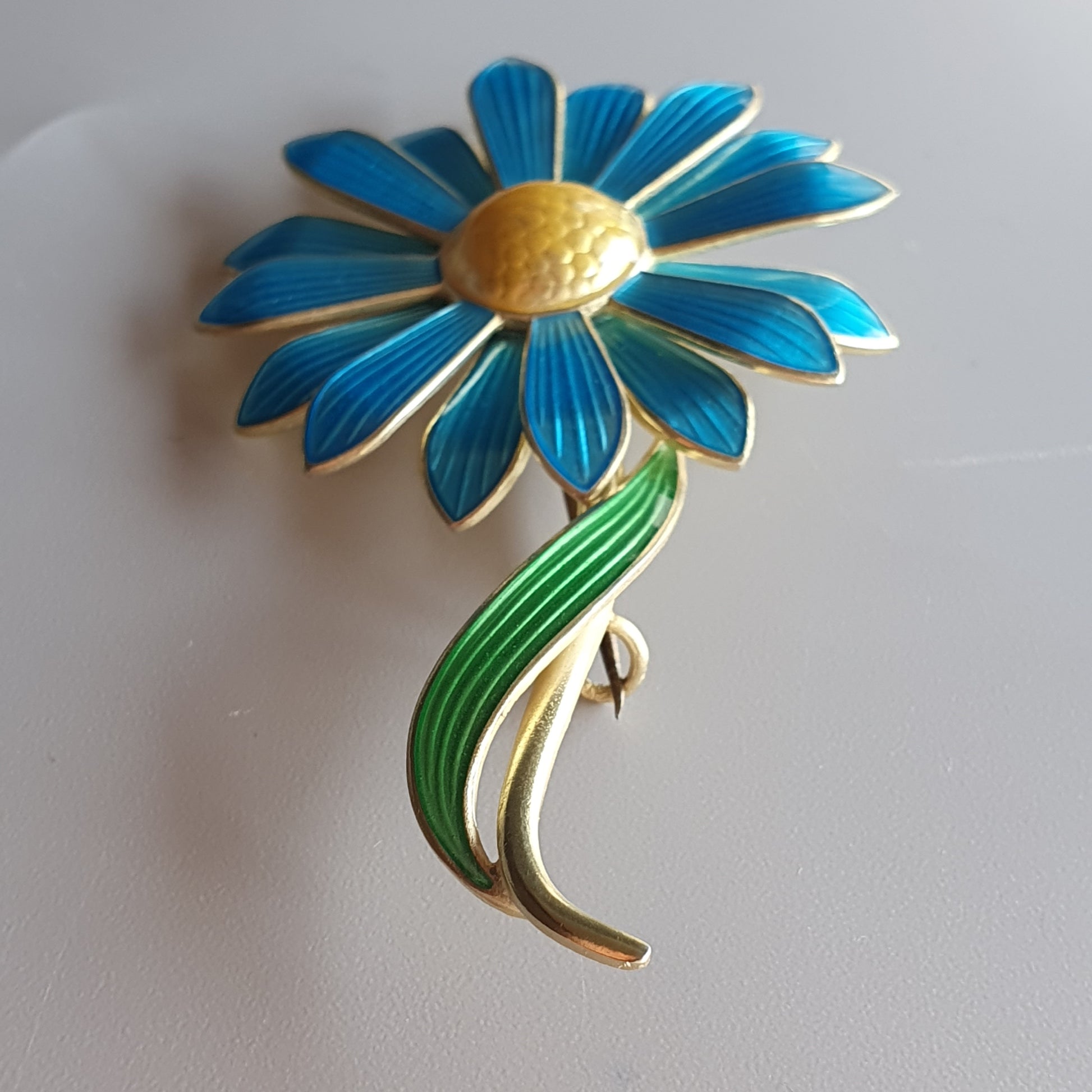 Colorful enamel flower brooch with blue petals and a green stem.