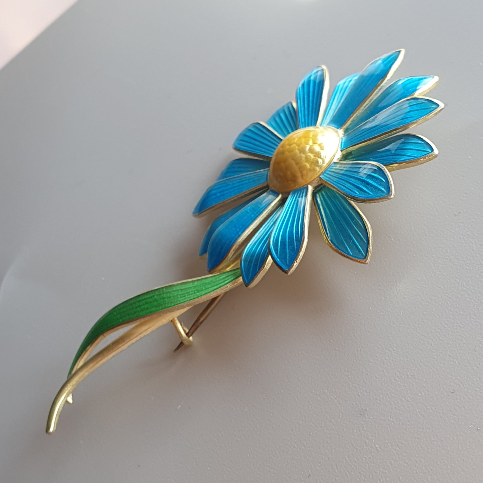 Bright blue and gold flower-shaped brooch with a green stem.