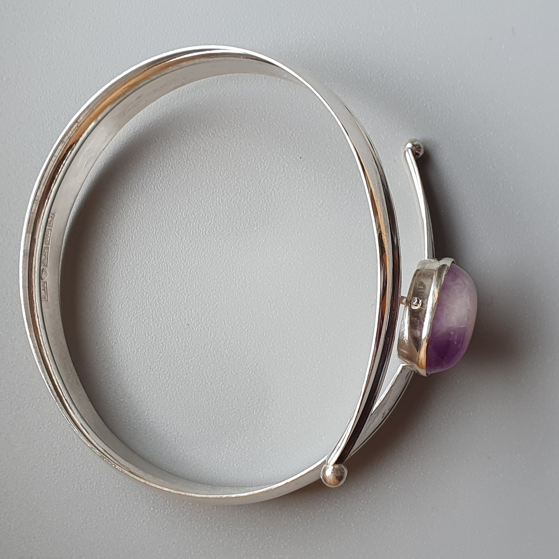 Silver bangle bracelet with a purple gemstone accent.