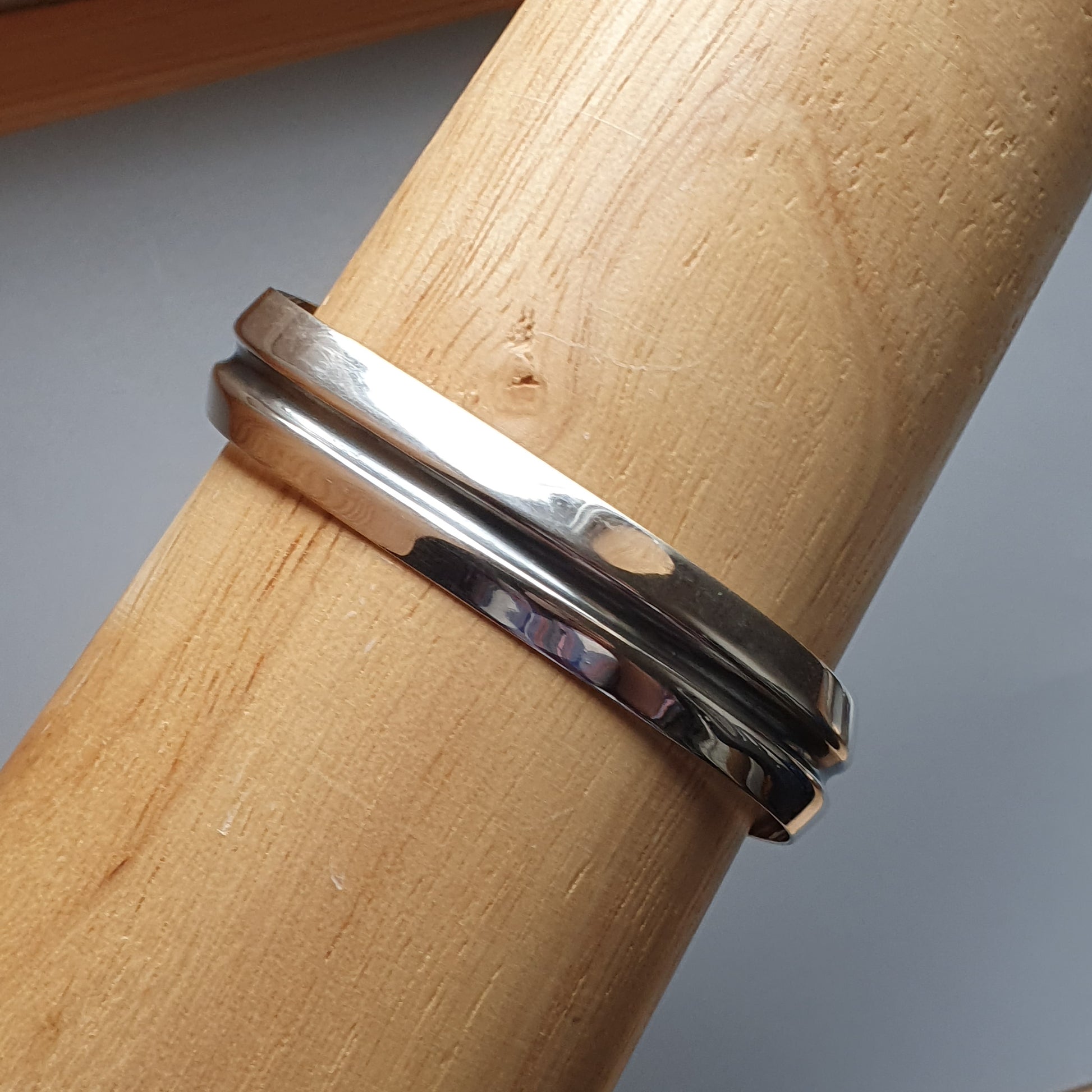 Silver ring with a simple, modern design worn on a wooden dowel or cylinder.