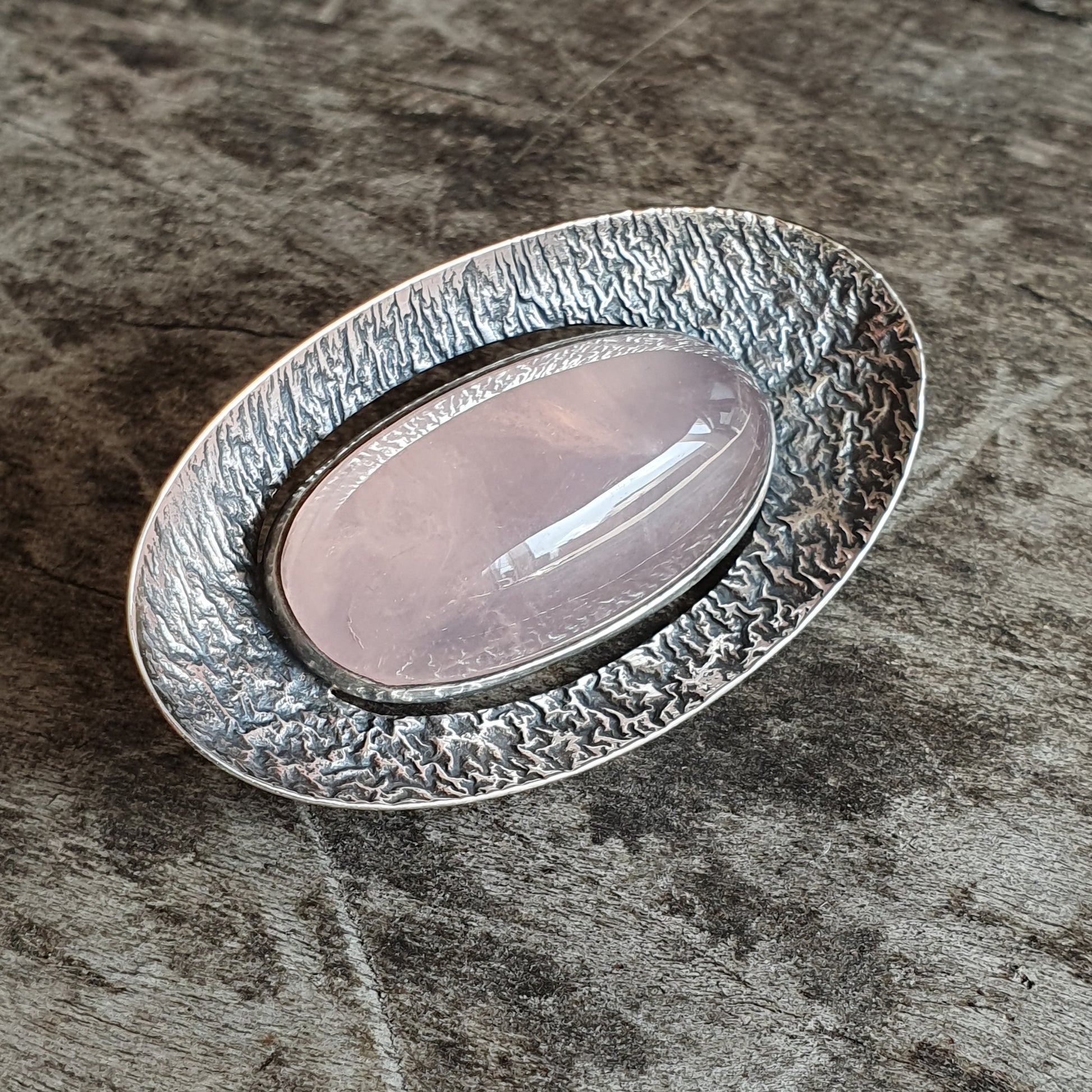 Silver brooch or pendant with an oval rose quartz stone set in a textured frame.