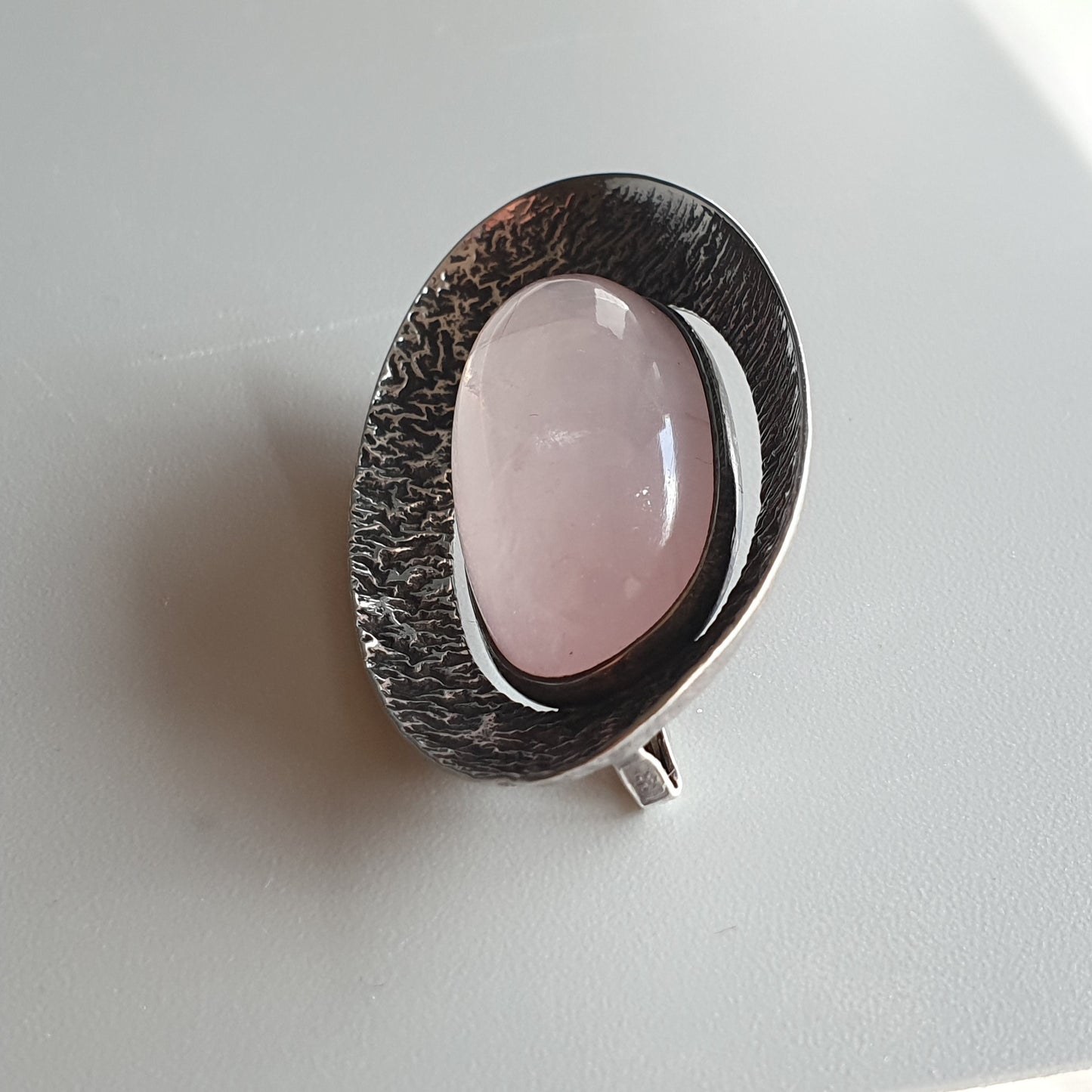 Oval-shaped silver pendant with a pink gemstone or cabochon set in the center.