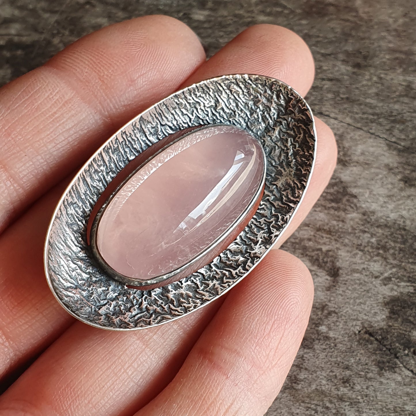 Oval silver pendant with a textured rim surrounding a smooth rose quartz stone.