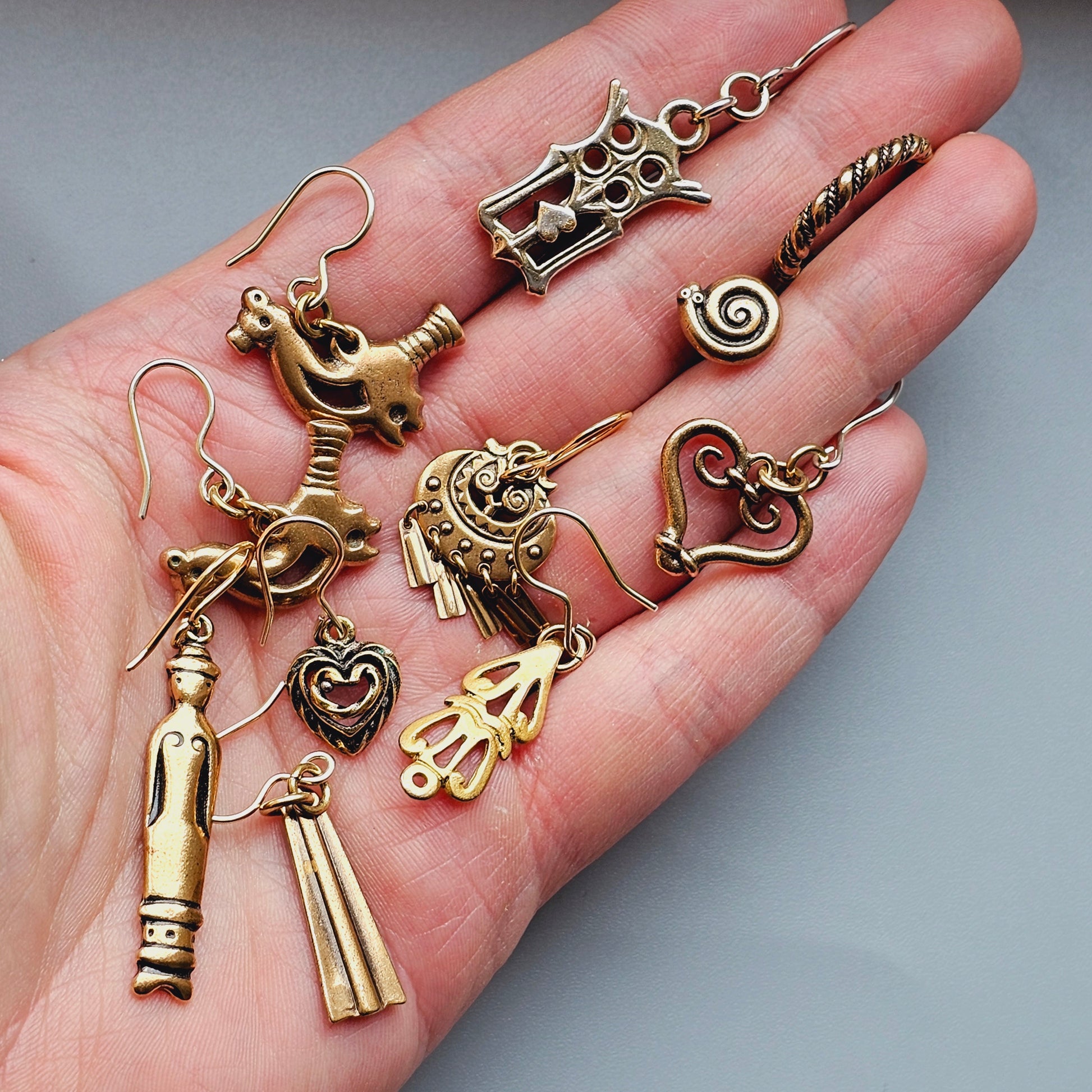 Hand holding various small metal charms and pendants.