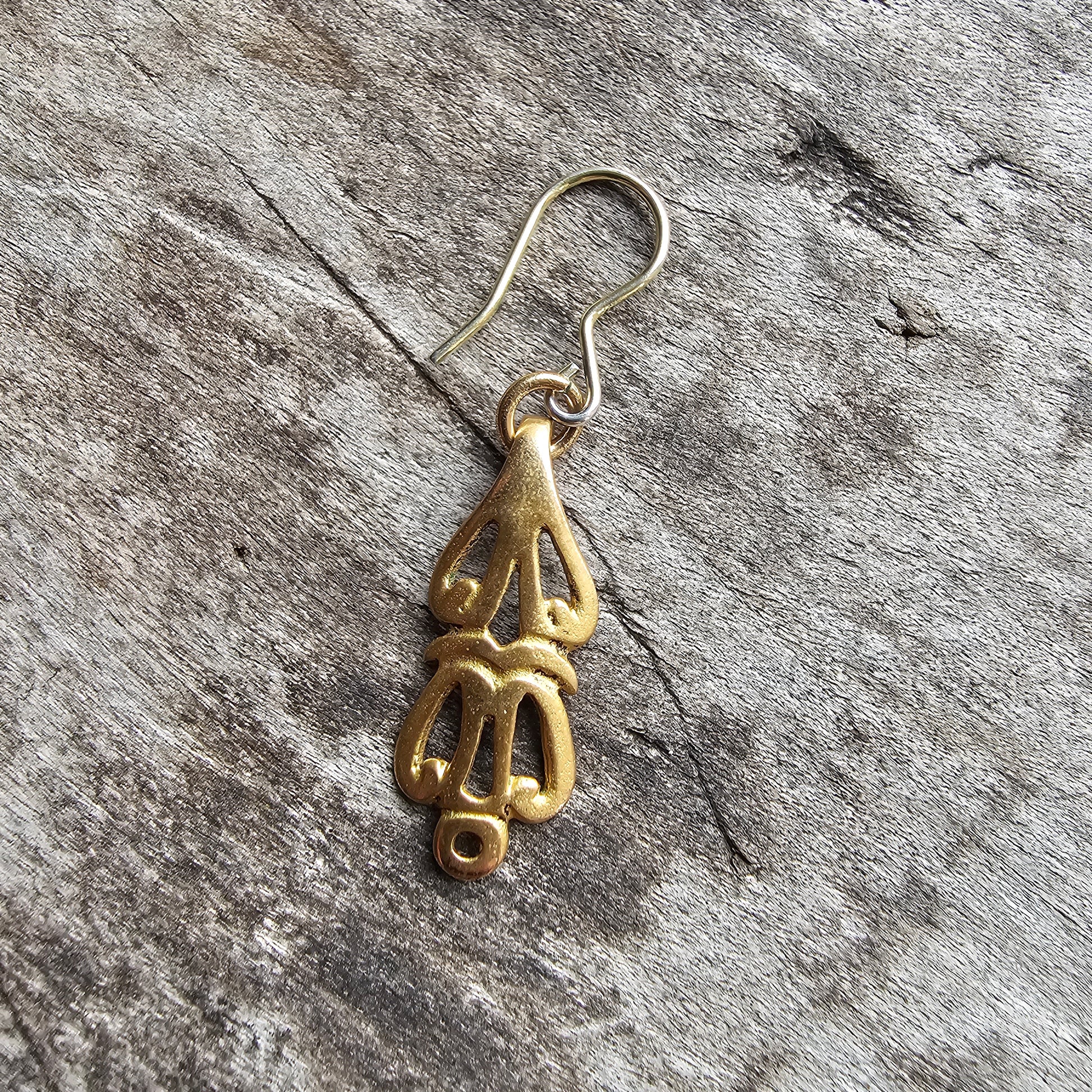 Gold-colored pendant or earring shaped like a stylized hand or hamsa symbol.