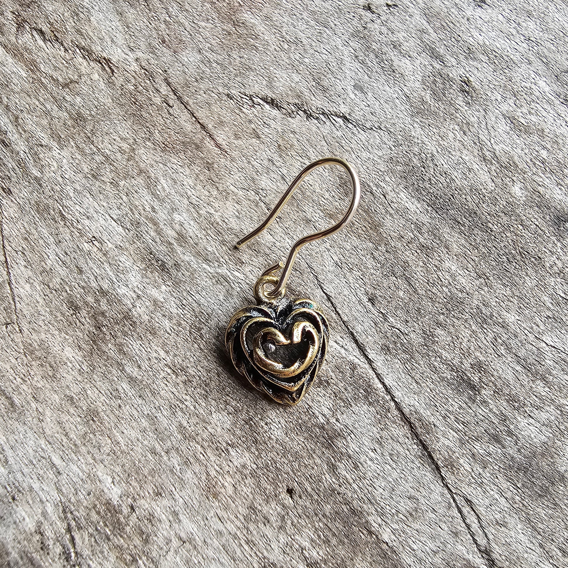 Heart-shaped metal earring or charm with an intricate swirled design.