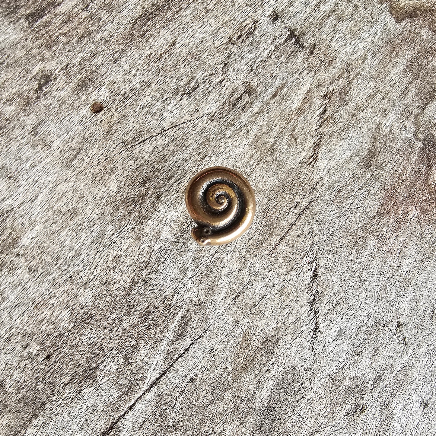 Spiral-shaped metal pendant or charm with a golden bronze color.