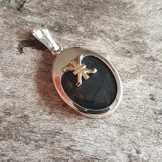 Silver pendant with a black oval stone featuring a gold cross design.