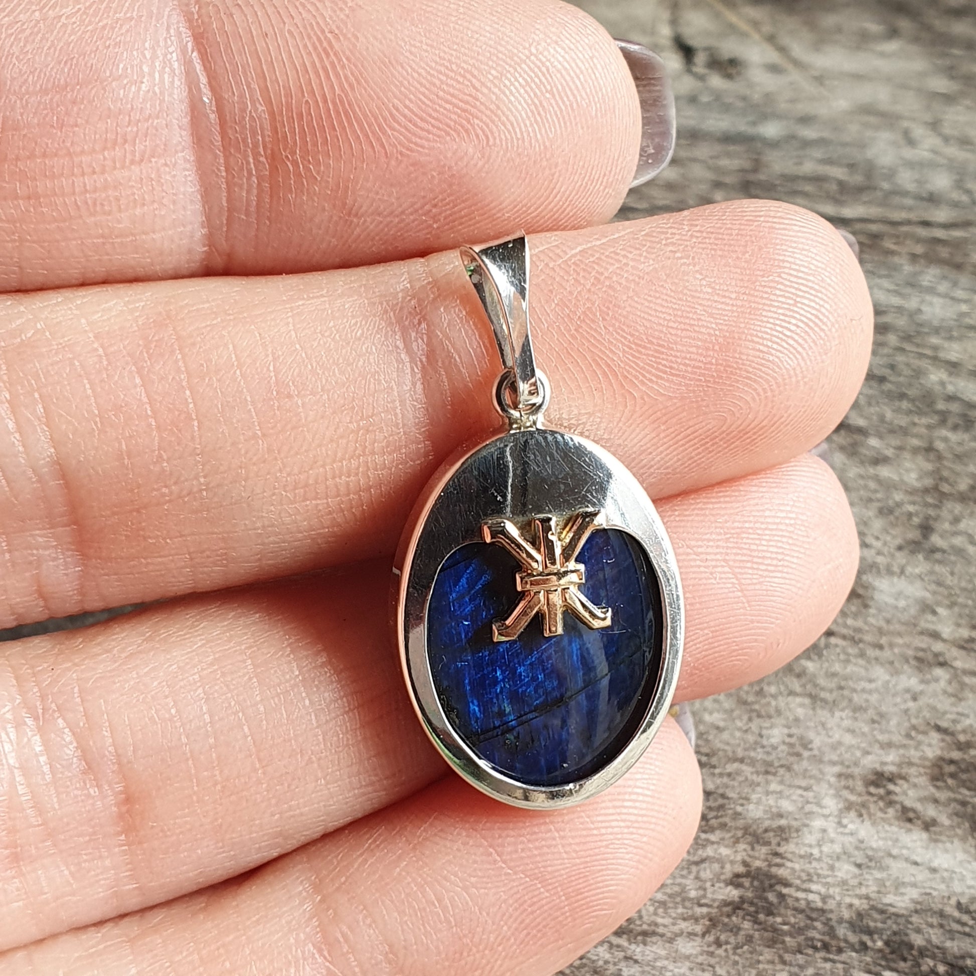 Silver pendant with an oval blue stone and a decorative symbol on top.