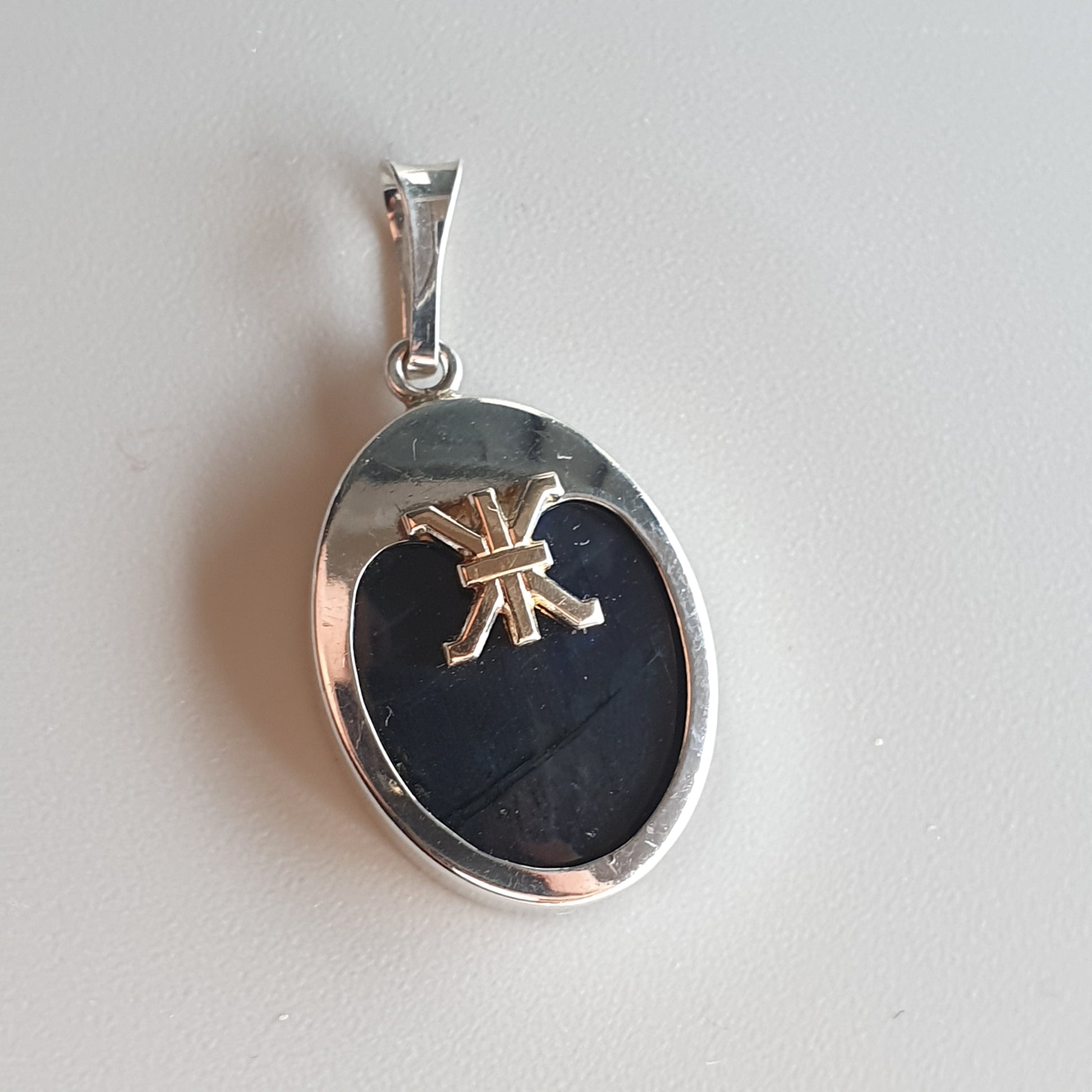 Silver pendant with an oval black stone and a small gold bow design.