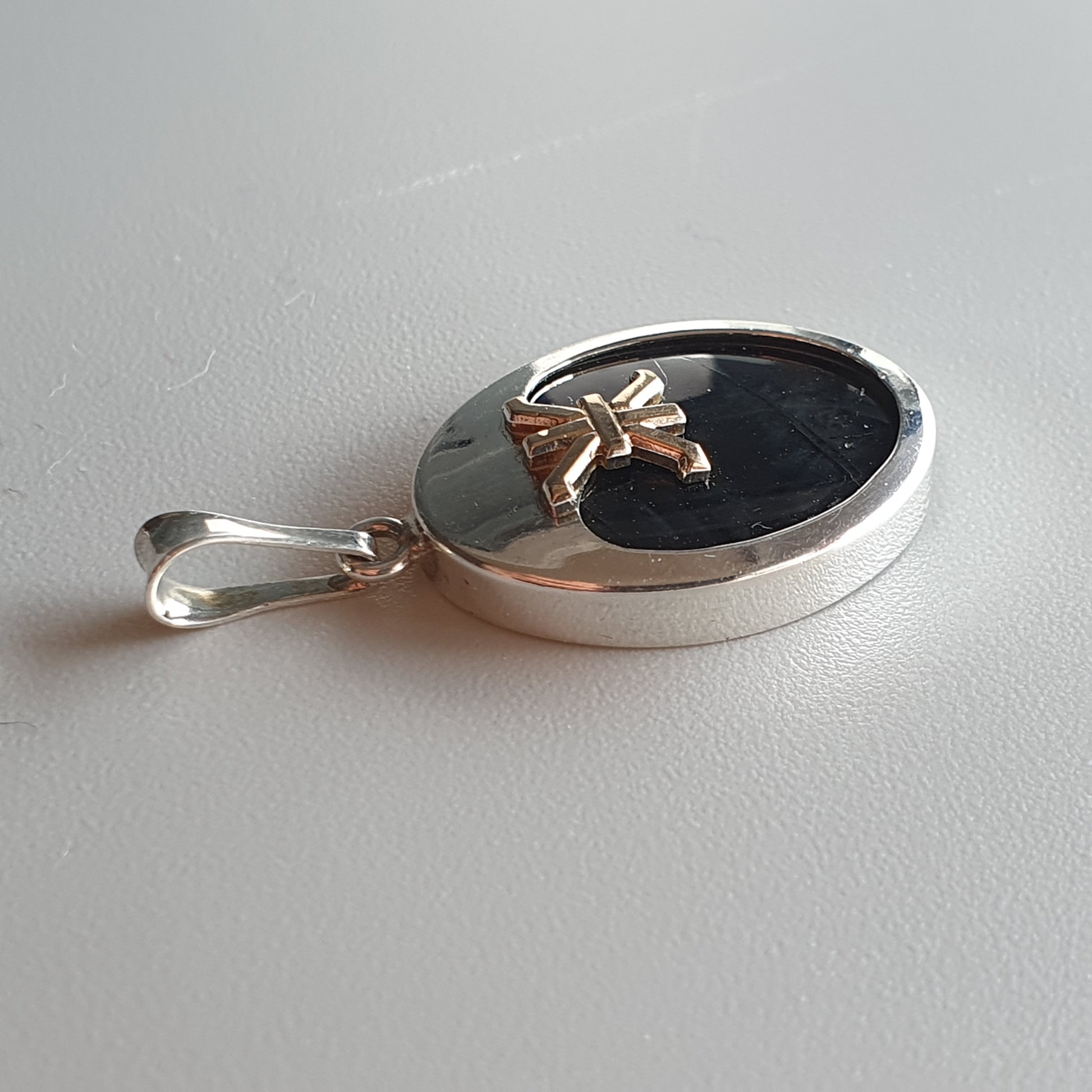 Silver pendant with a circular black inlay and a small gold cross accent.