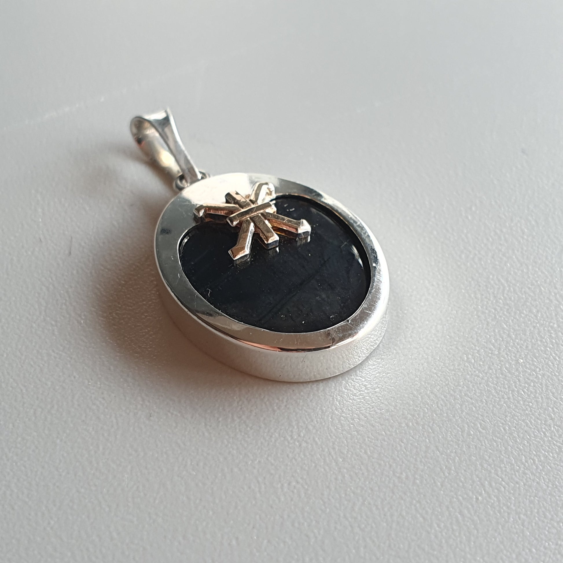 Silver pendant with a black oval center and a small gold-colored bow decoration.