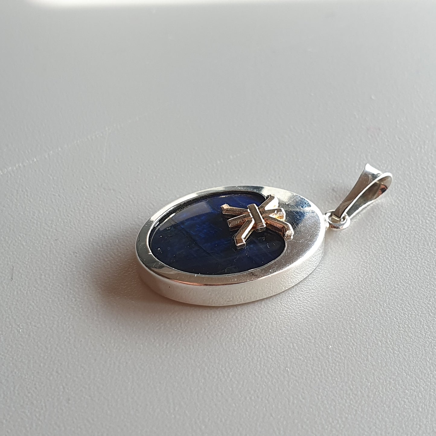 Silver pendant with an oval blue stone and a small bow-shaped accent.