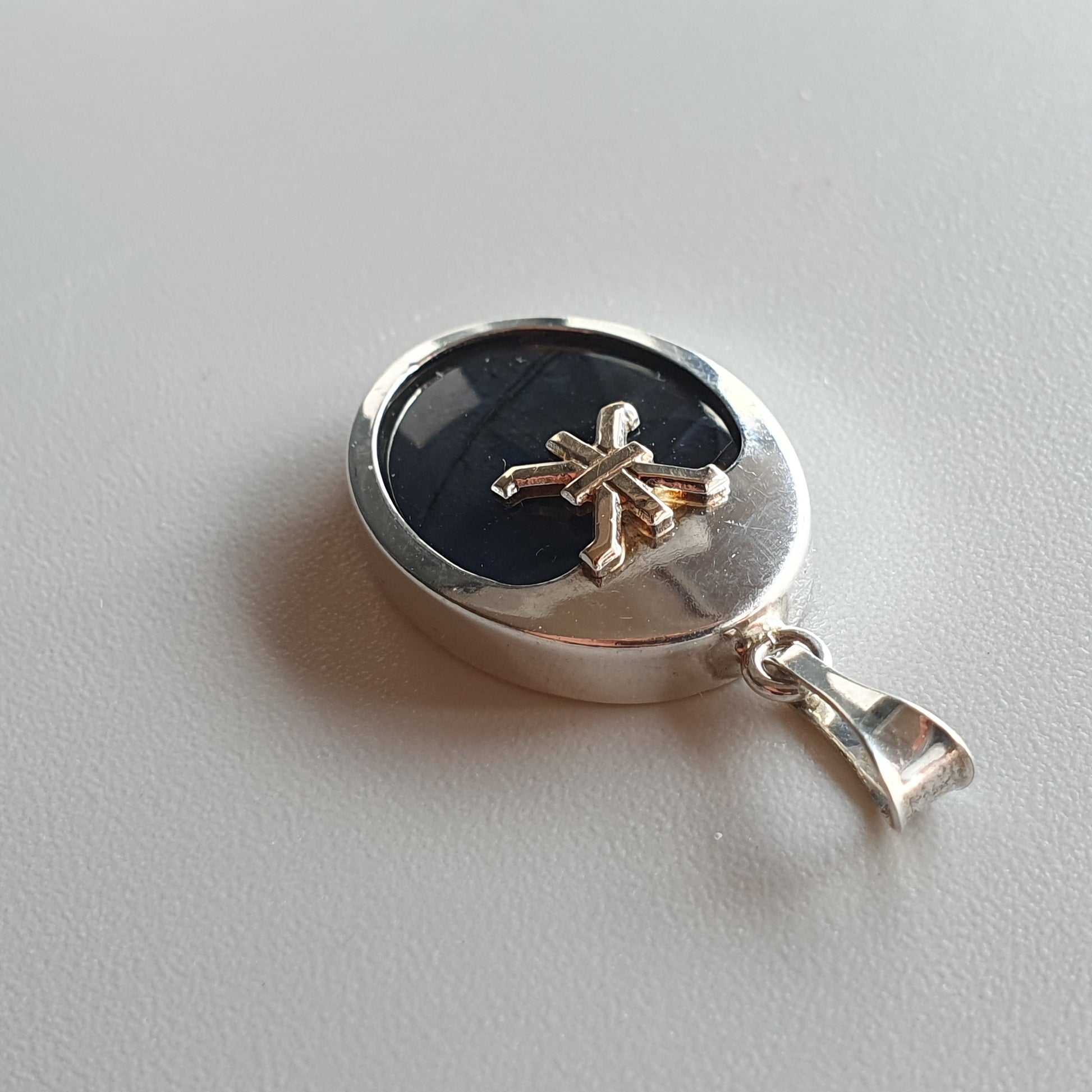 Silver pendant with a black center and a gold starfish or flower design.