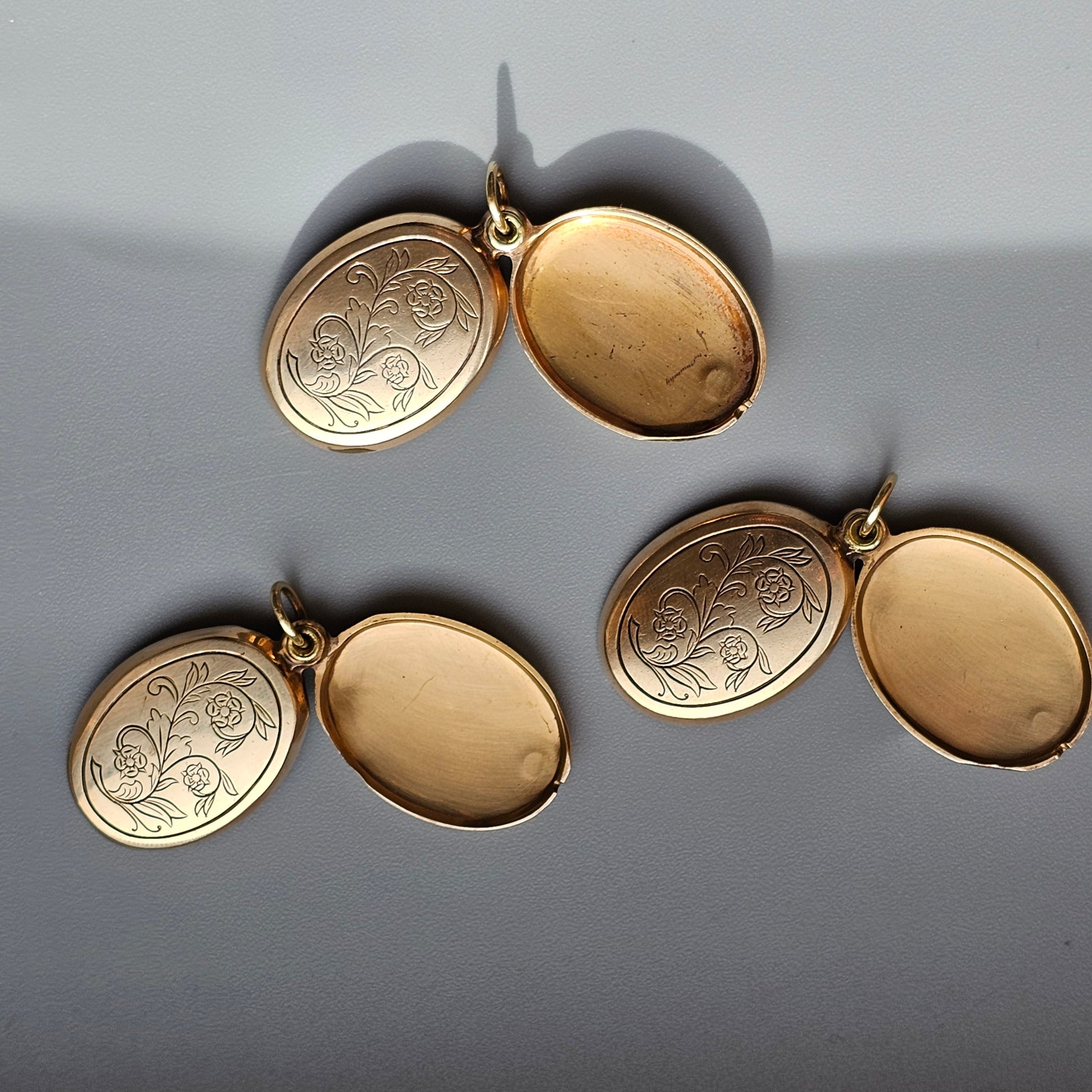 Gold lockets with engraved designs on one side.