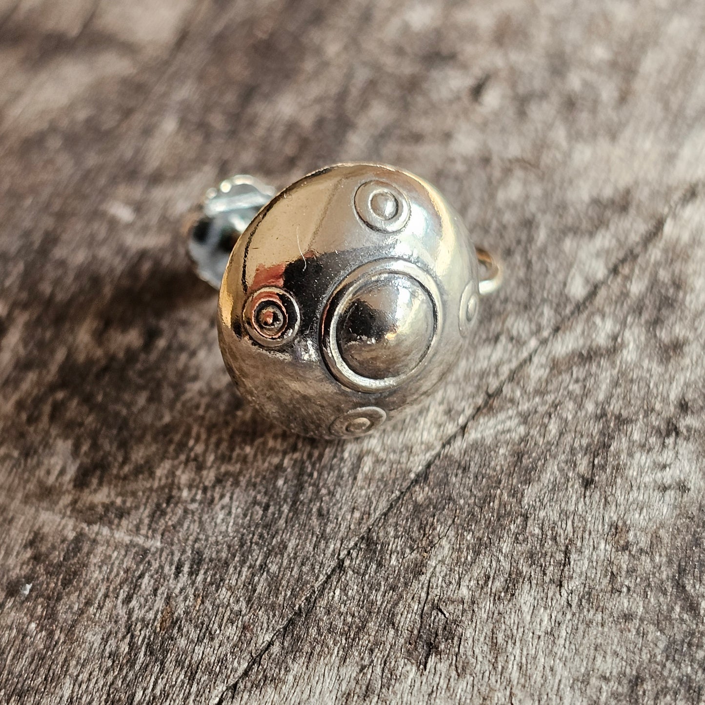 Metallic spherical bead or charm with circular indentations and a small screw.