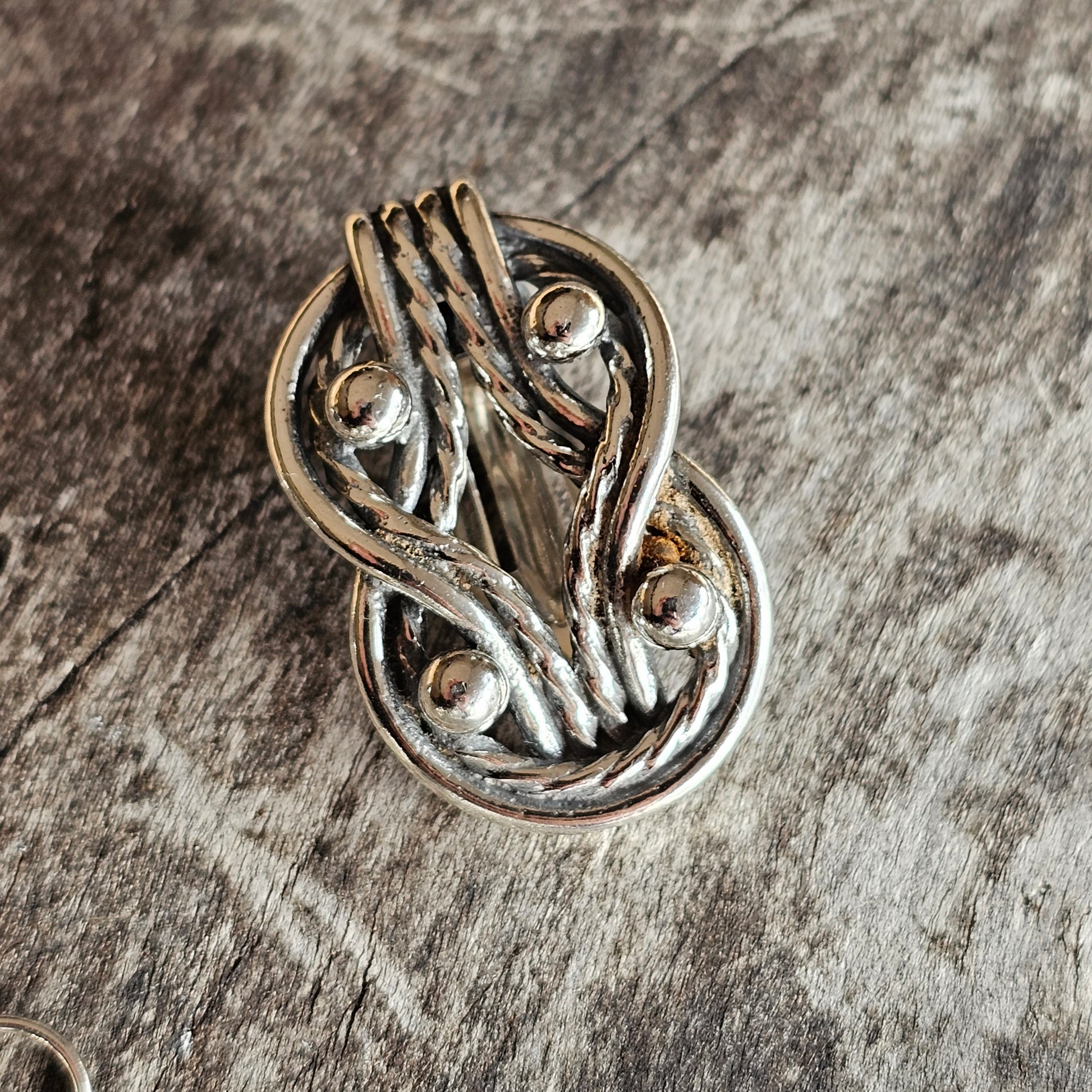 Intricately designed silver brooch or pendant with swirling metalwork and small spherical elements.