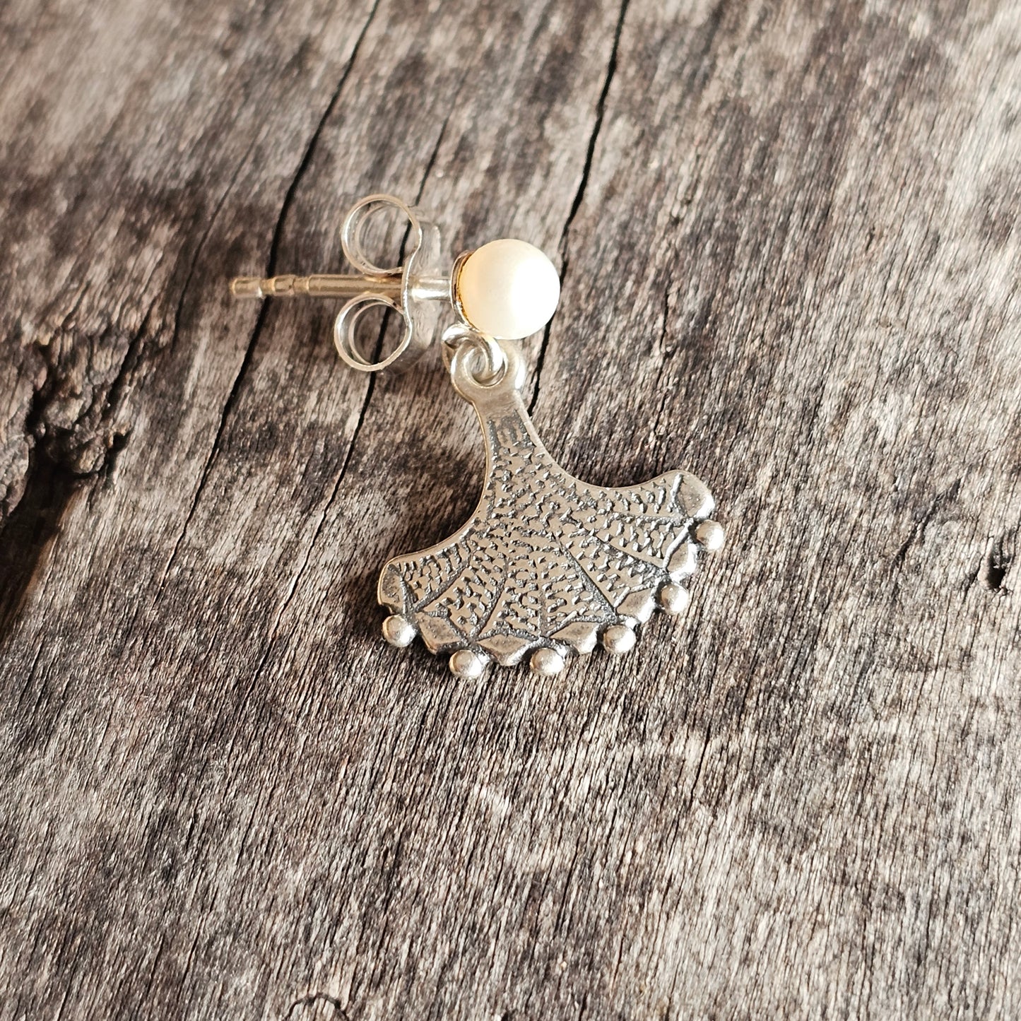 Ornate silver earring with a fan-shaped design and small dangling beads.