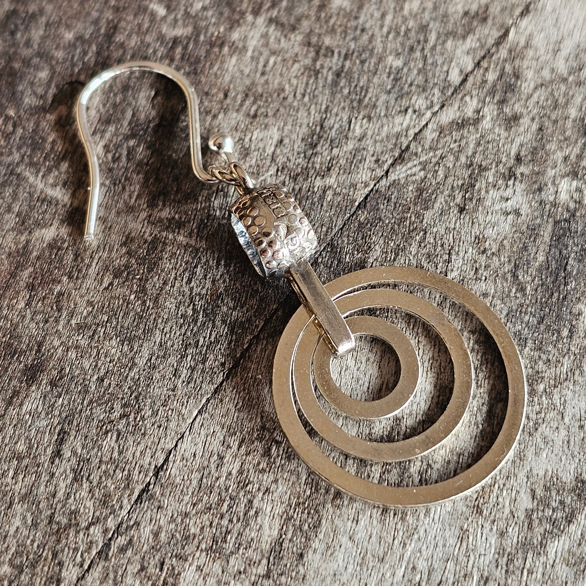 Spiral-shaped silver earring with a hook and decorative bead.