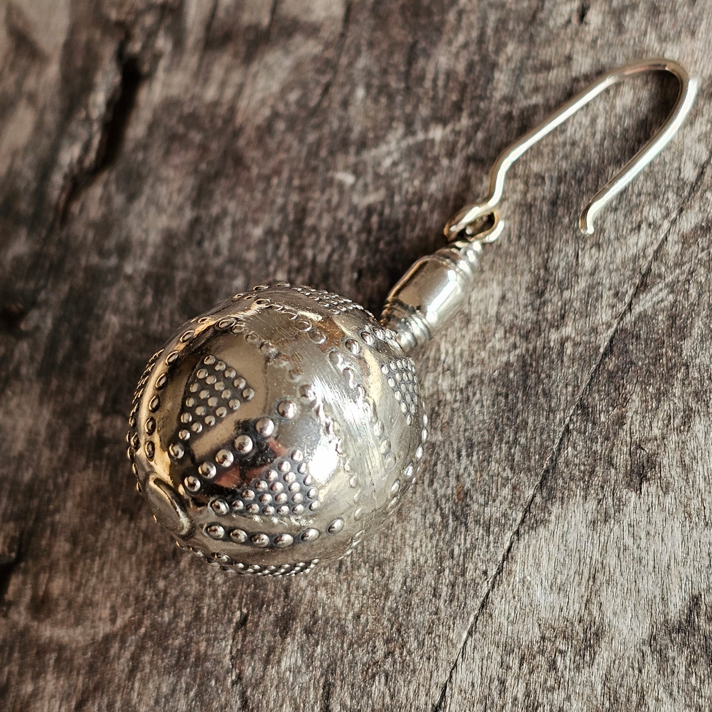 Ornate silver spherical earring with intricate perforated patterns.