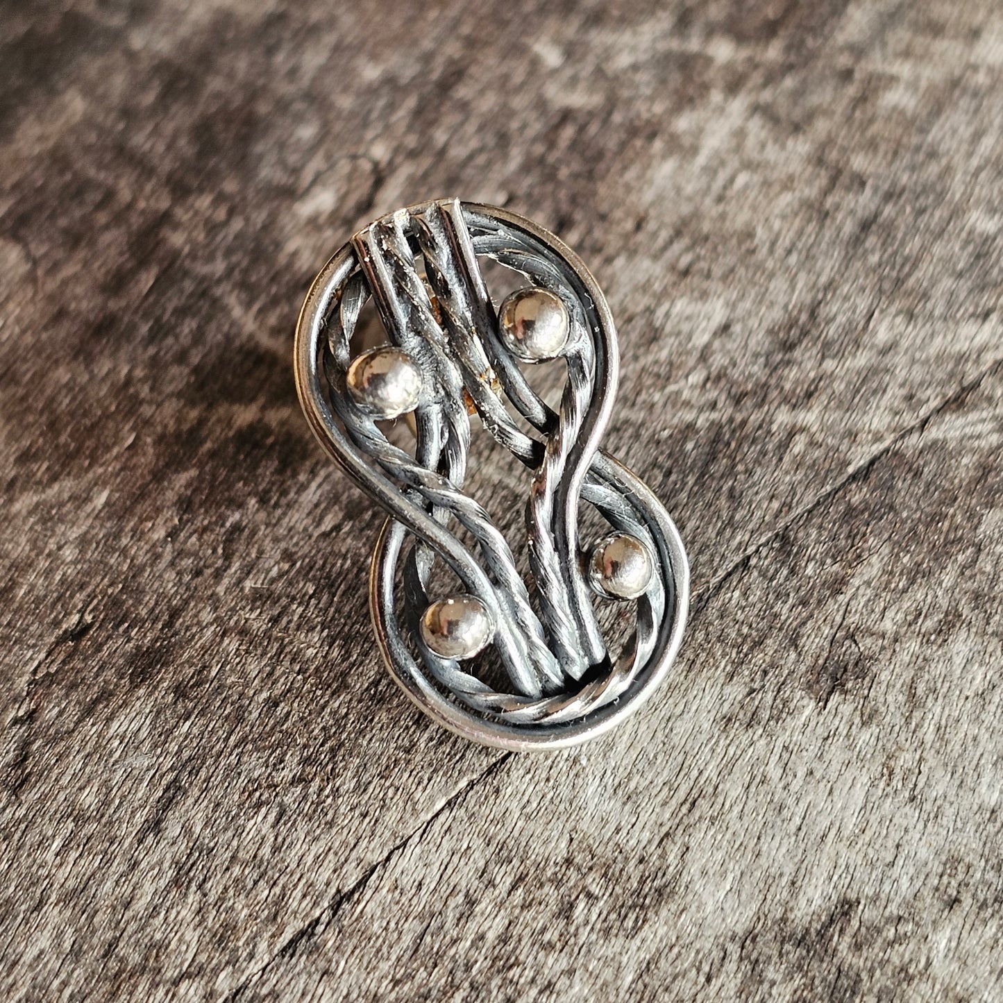 Silver-toned metal brooch or pin with an intricate figure-eight or infinity symbol design.