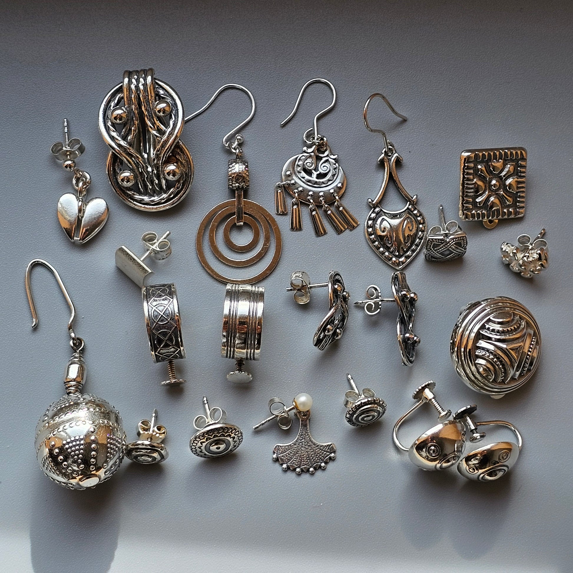 Collection of silver-toned jewelry pieces and components including earrings, pendants, and charms.