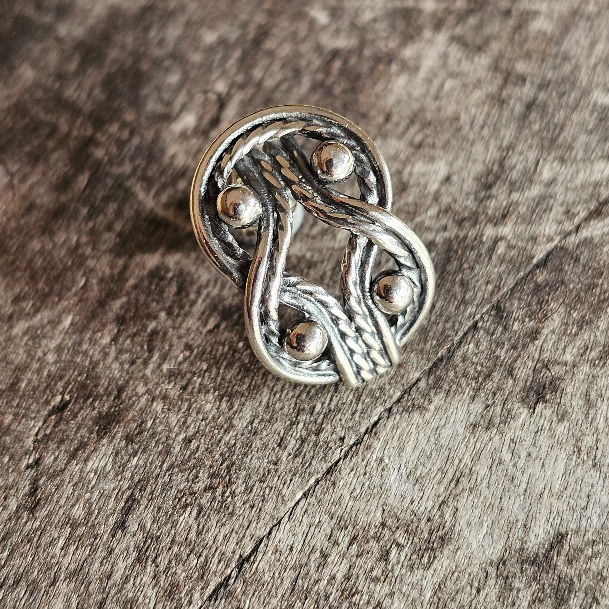 Silver metallic pin or brooch with an intricate knotted design.