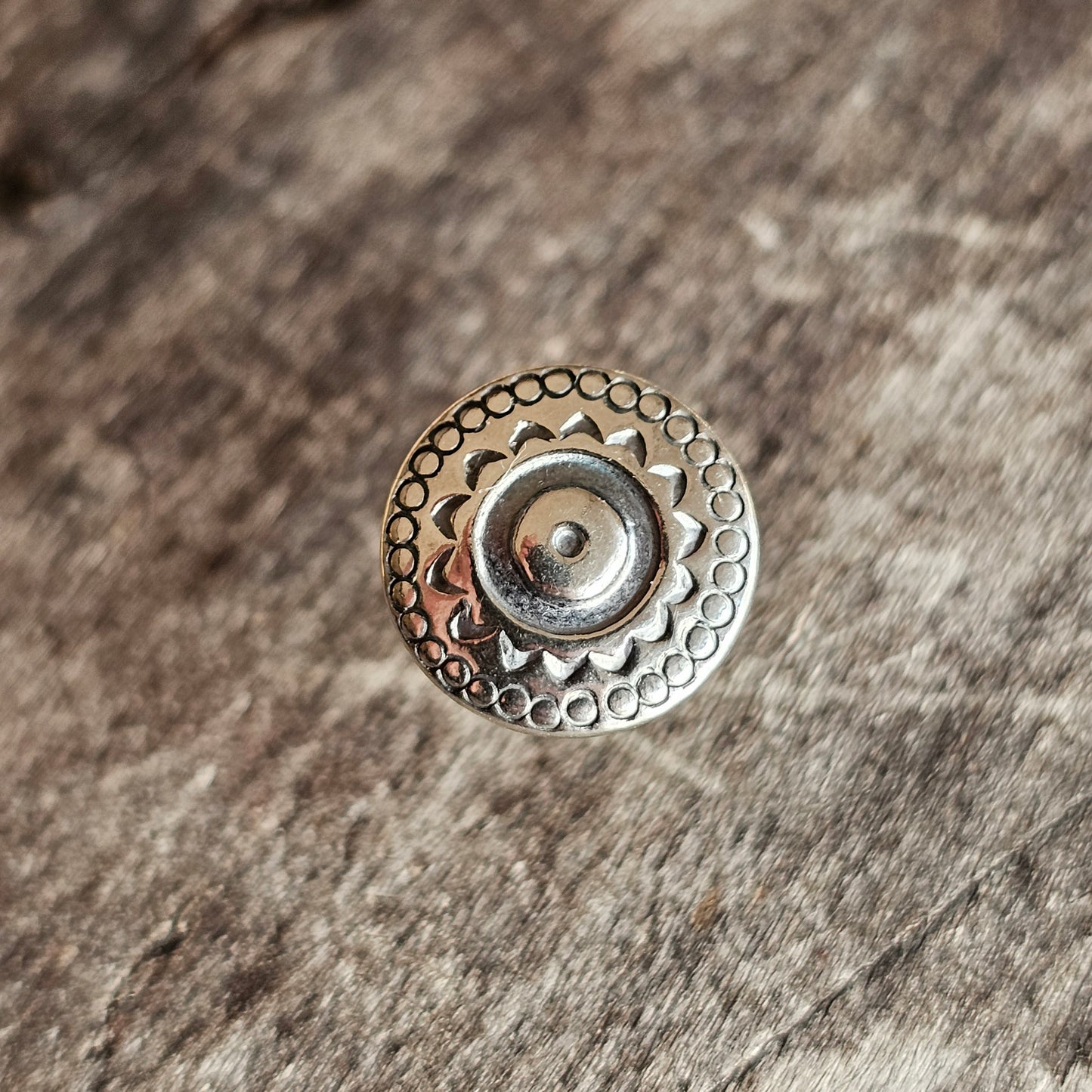 Decorative metal button with circular patterns and a central dome.