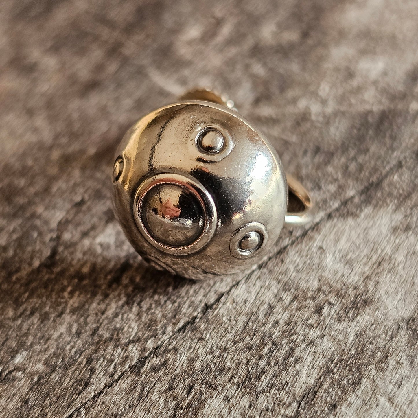 Silver ring with circular designs and a small opening revealing a reddish interior.