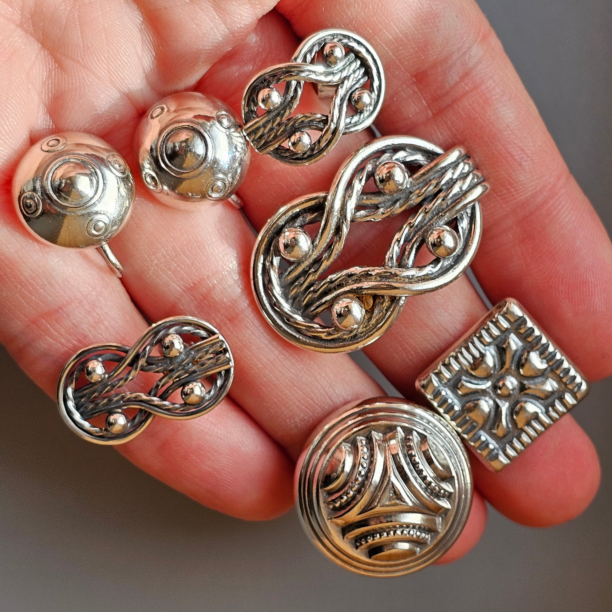 Collection of ornate silver metal buttons or jewelry components held in an open palm.