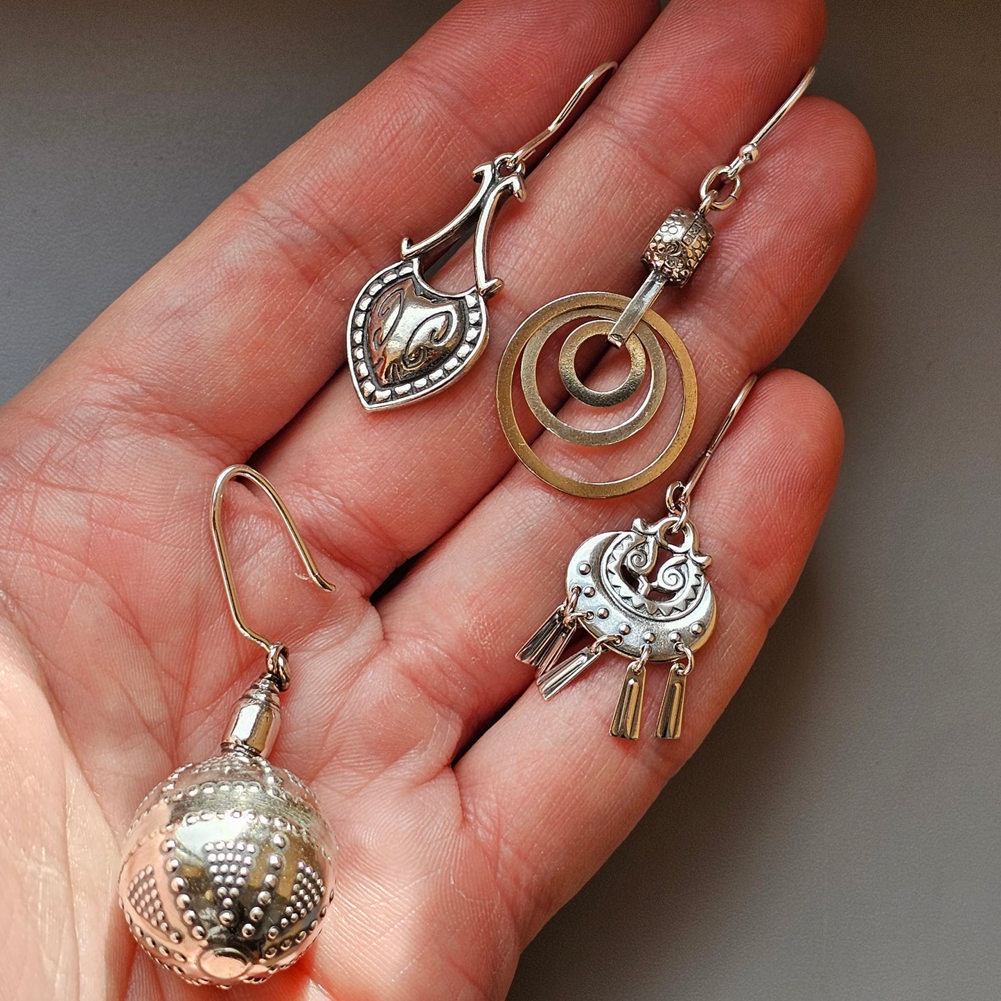 Hand holding various decorative earrings and pendants.