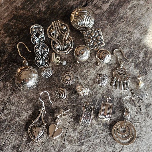 Collection of silver-toned jewelry pieces and ornaments with various designs and shapes.