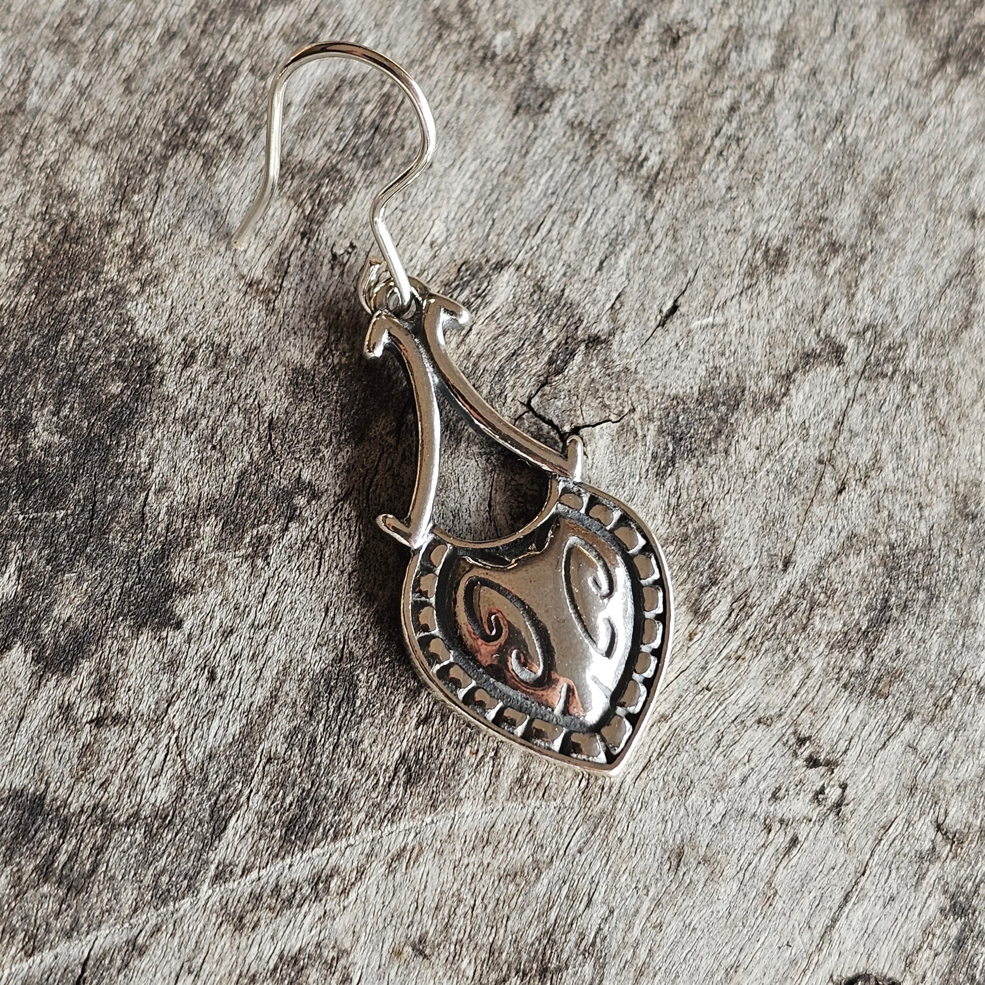 Heart-shaped silver pendant earring with decorative swirl pattern.