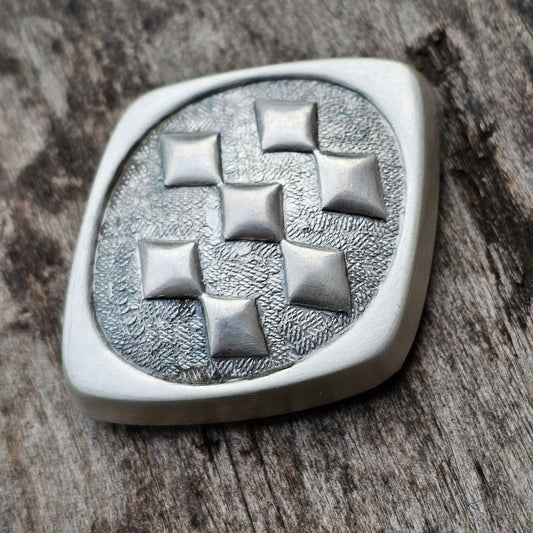 Silver-colored metal brooch or pin with a geometric diamond pattern.