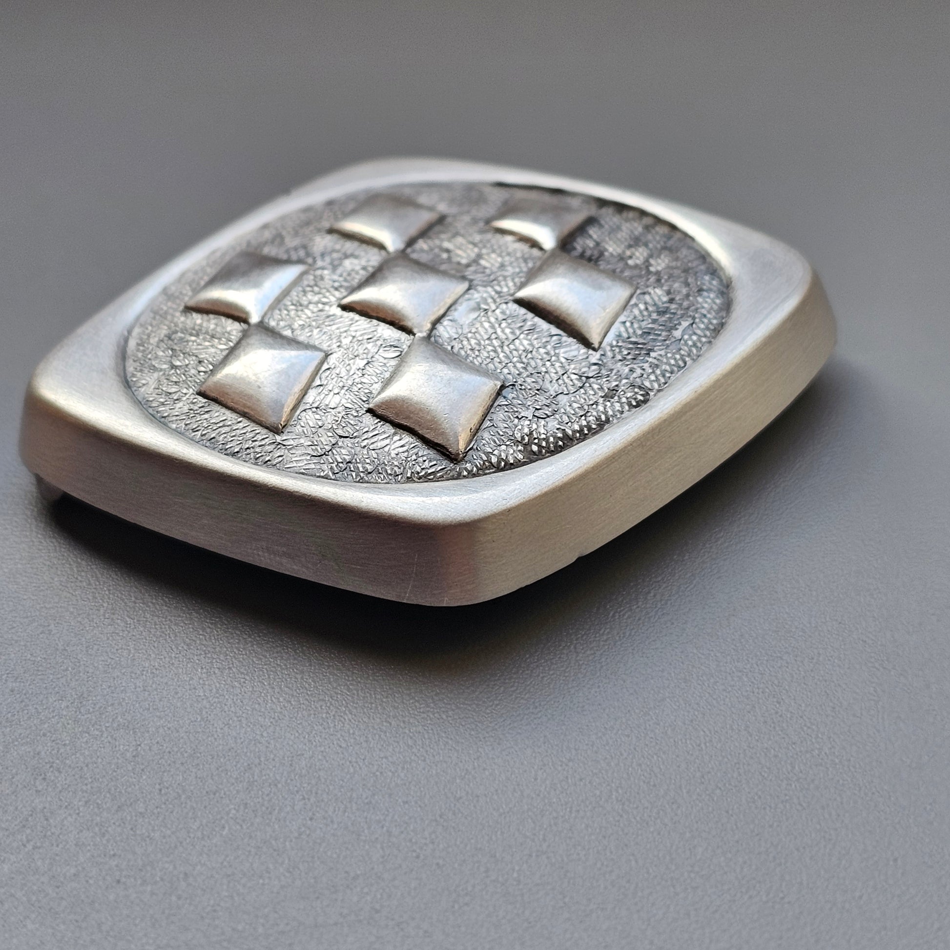 Square metal belt buckle with a quilted pattern of raised studs.