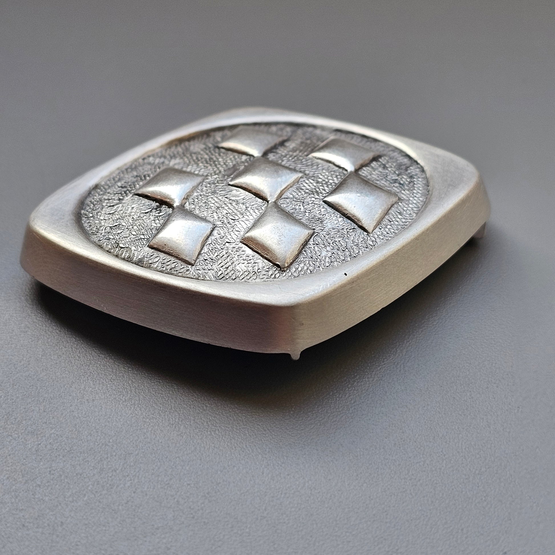 Silver belt buckle with a textured checkerboard pattern.