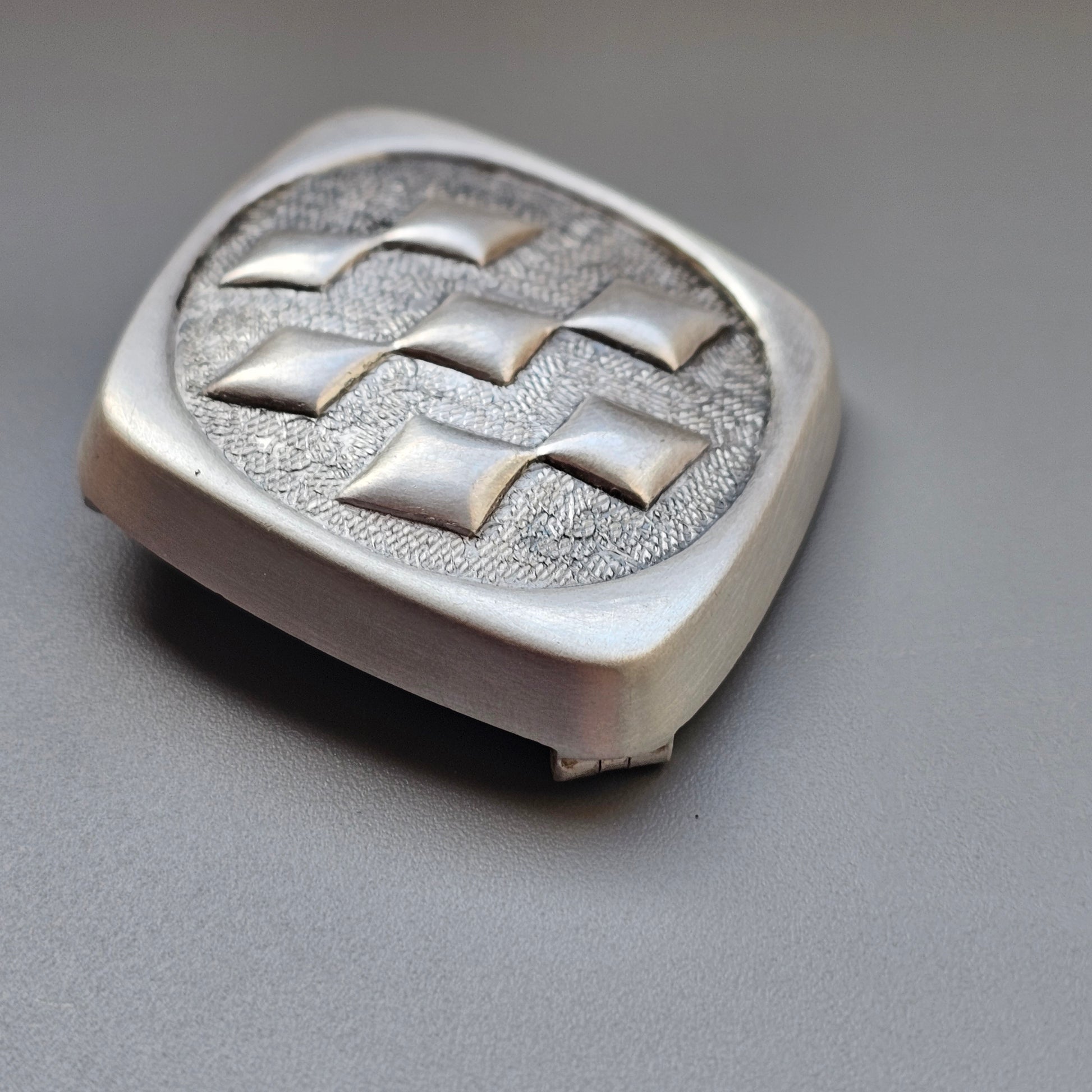 Silver-colored square button with a raised geometric pattern of diamond shapes.