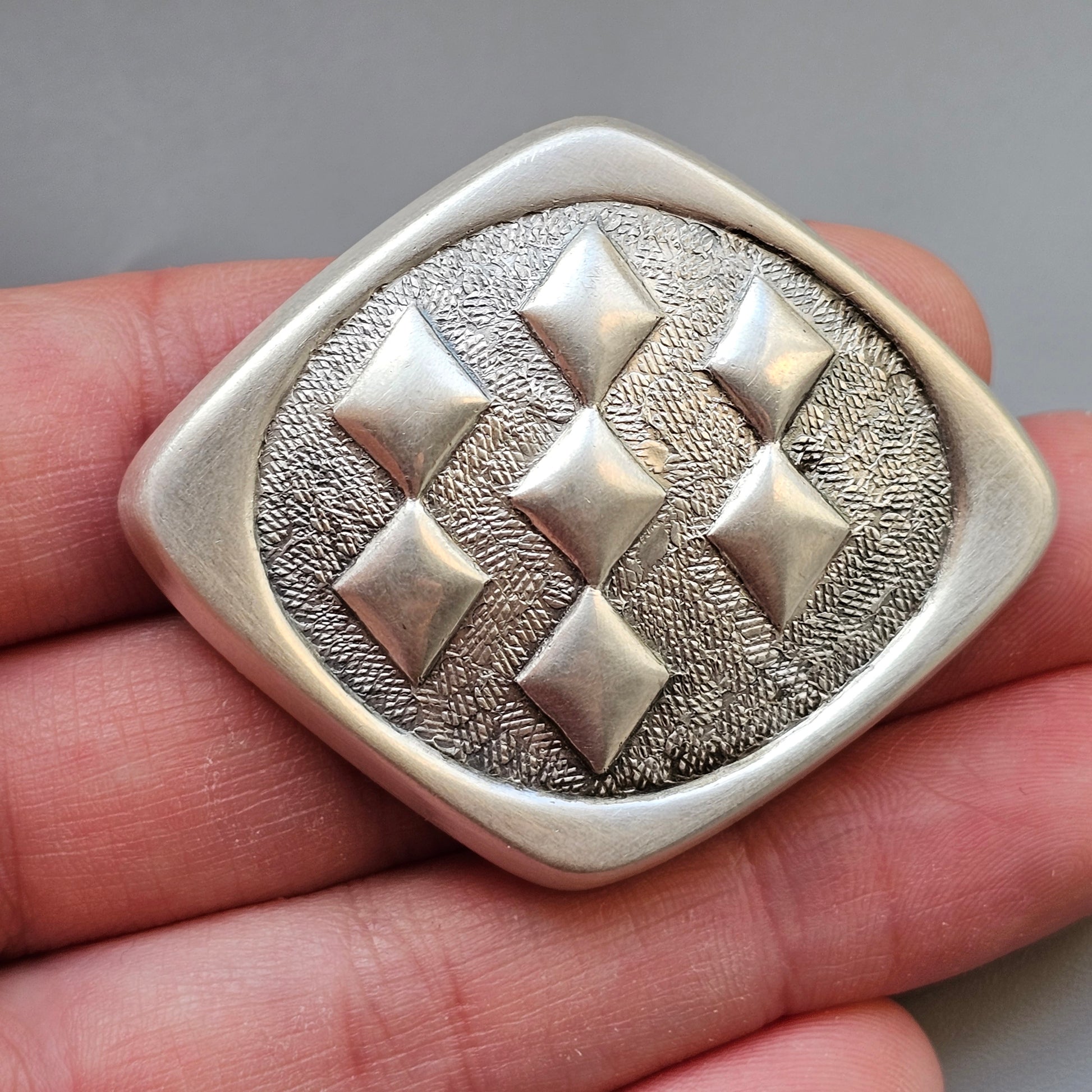 Silver brooch or pendant with a diamond-shaped design featuring raised geometric patterns.