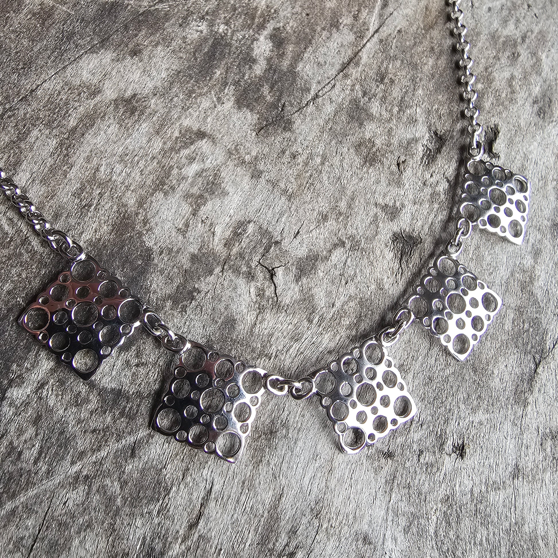 Silver necklace with geometric pendant pieces featuring honeycomb-like patterns.