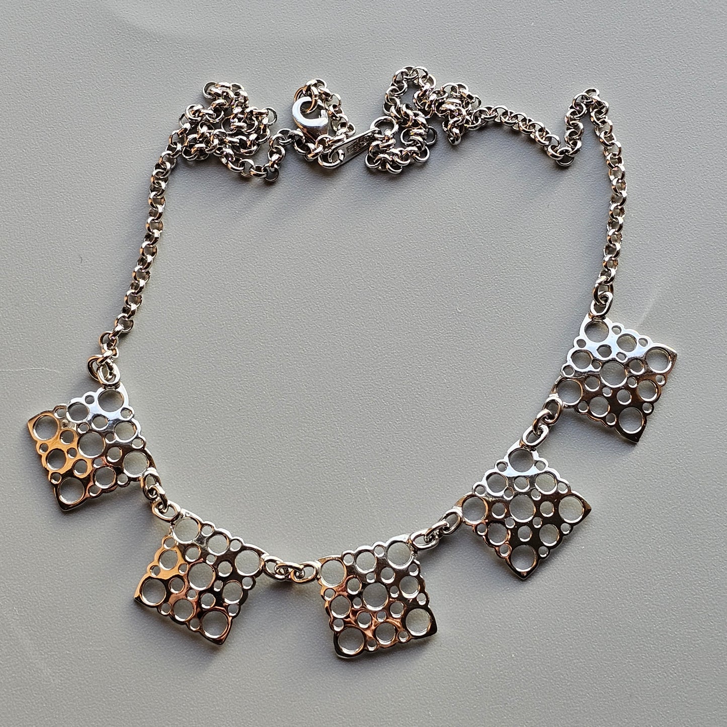 Silver necklace with five square pendants featuring circular patterns.