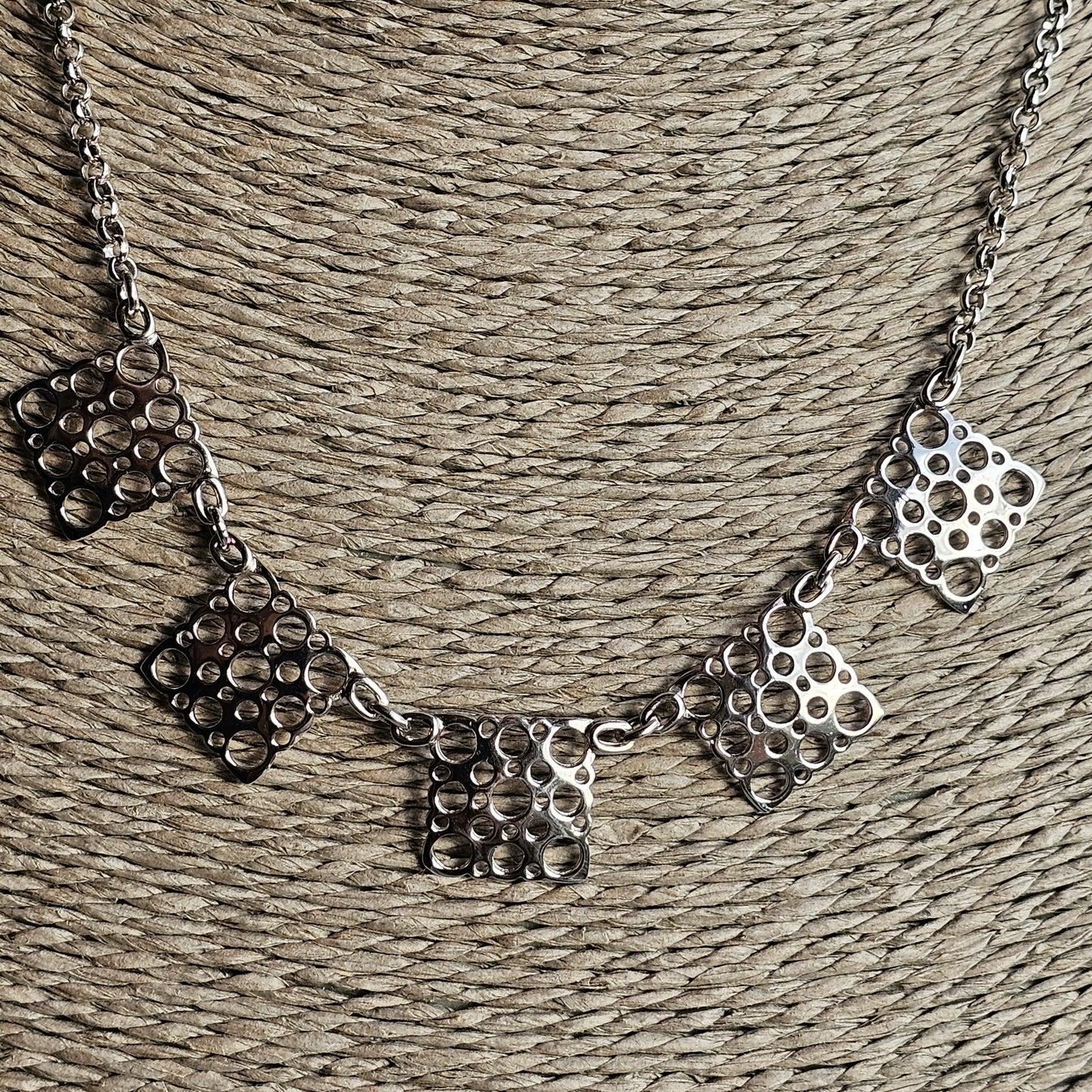 Metallic necklace with geometric pendant charms featuring circular patterns.