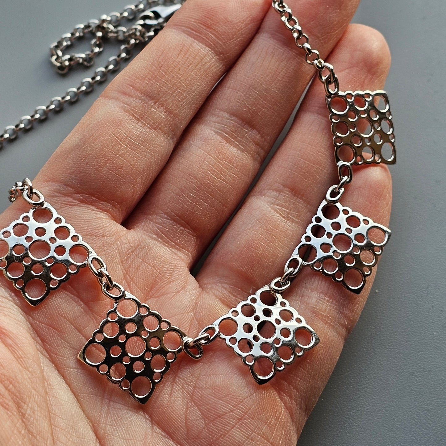 Silver necklace with geometric cutout square pendants.