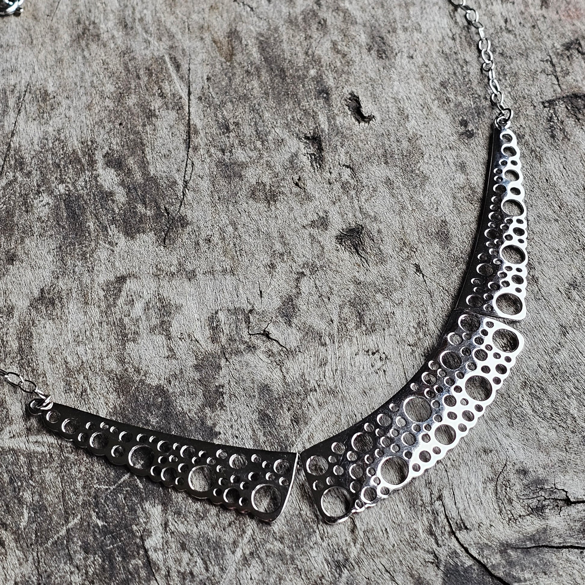 Silver necklace with a pattern of circular cutouts.